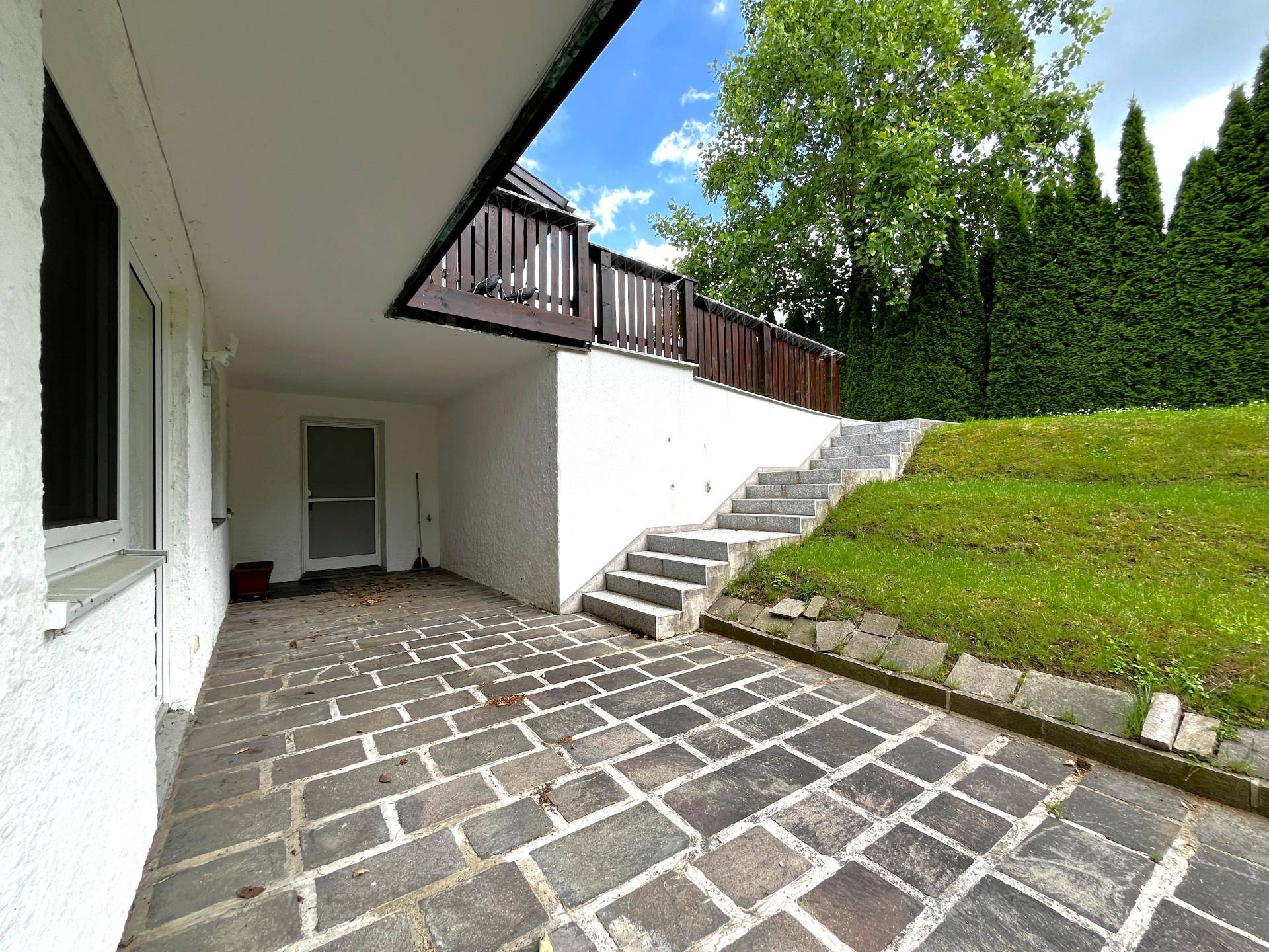 Überdachte Terrasse mit Steinplatten und Treppe zum oberen Balkon.