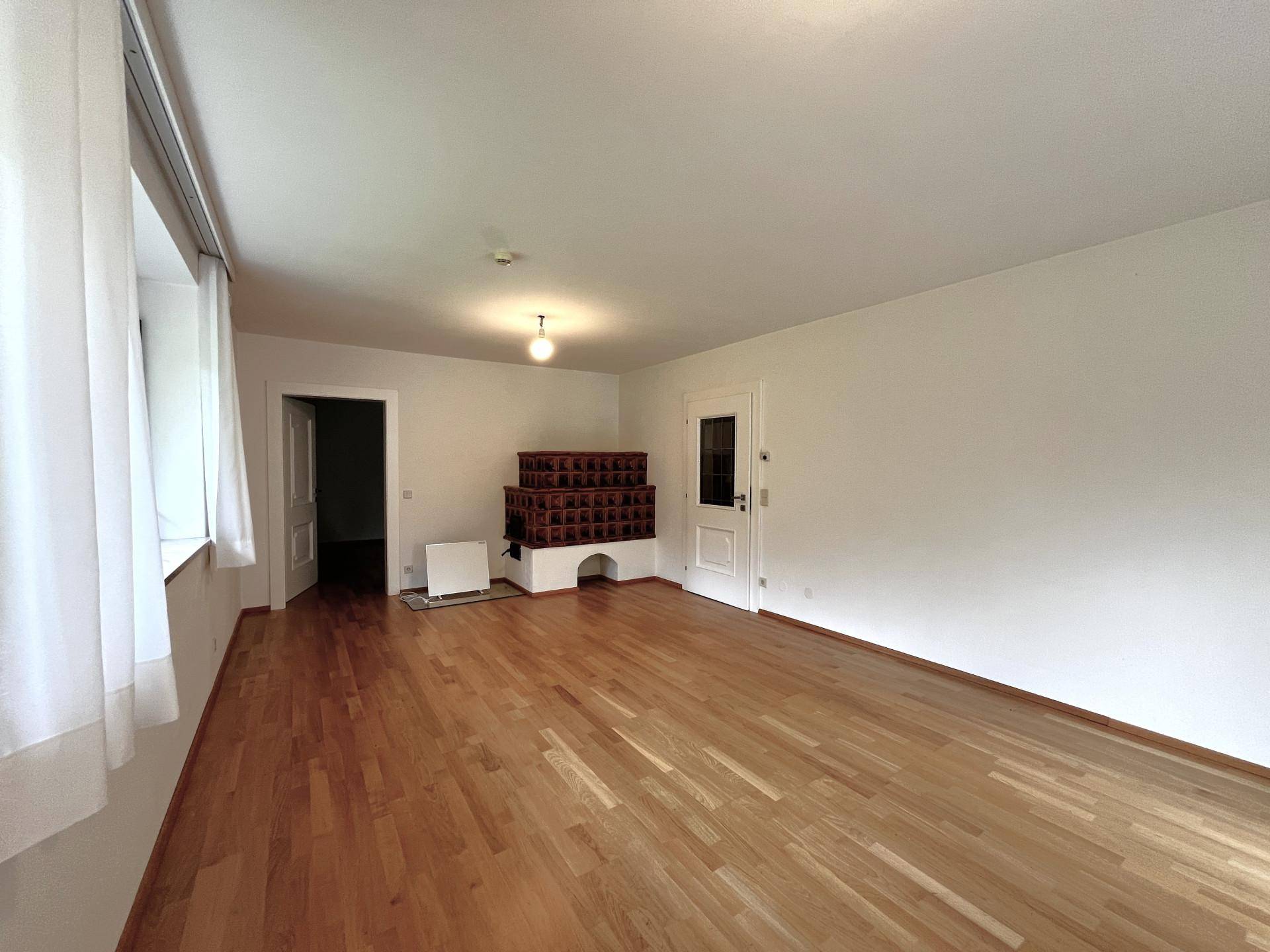 Geräumiges Wohnzimmer mit Holzboden und einem traditionellen Kachelofen.