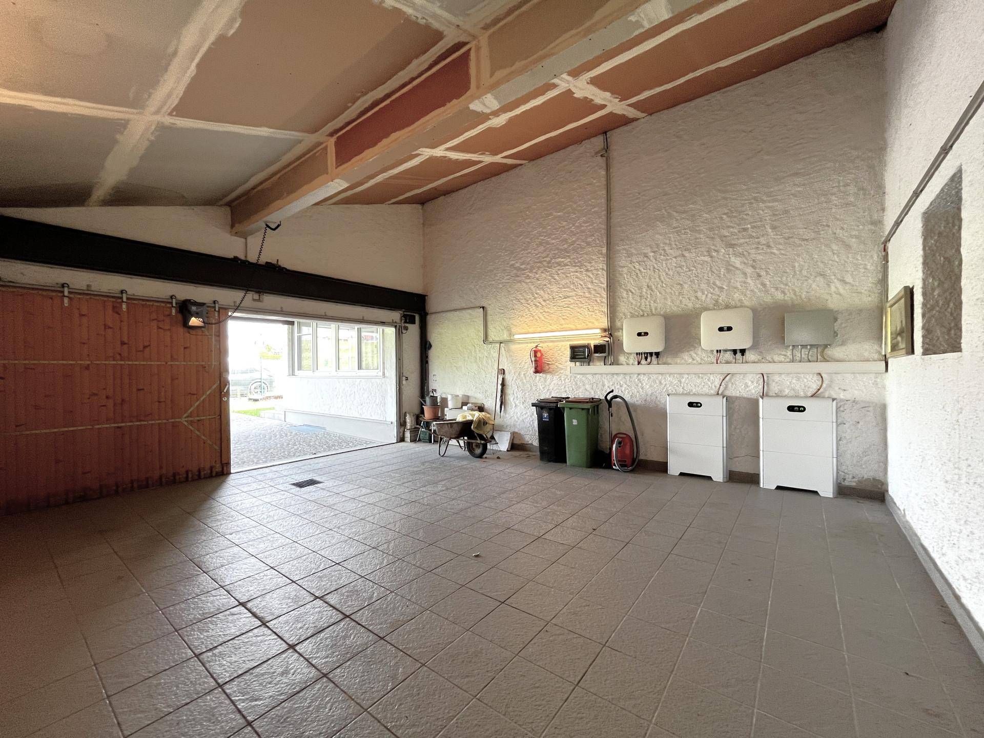 Geräumige Garage mit Fliesenboden und Photovoltaik-Wechselrichtern an der Wand.