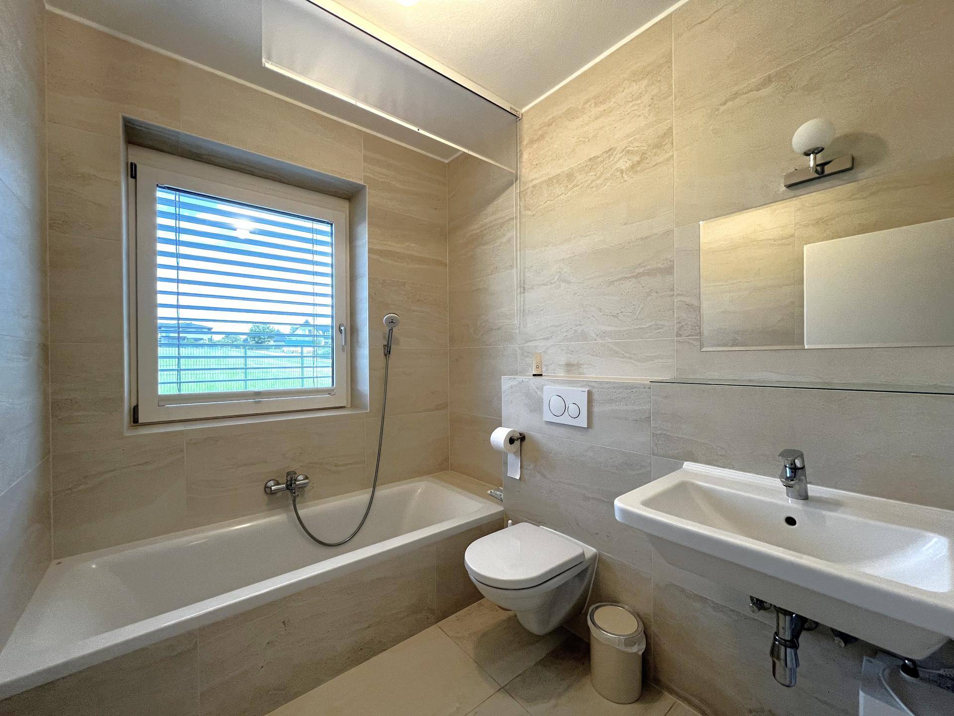 Modernes Badezimmer mit Badewanne, WC, Waschbecken und Fenster mit Blick ins Grüne.