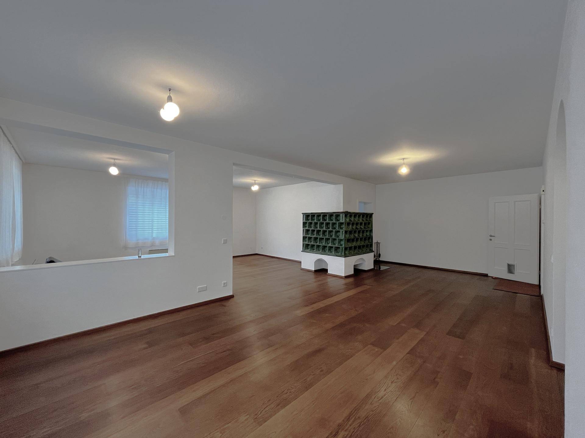 Helles Wohnzimmer mit Holzboden und traditionellem Kachelofen als zentrales Element.