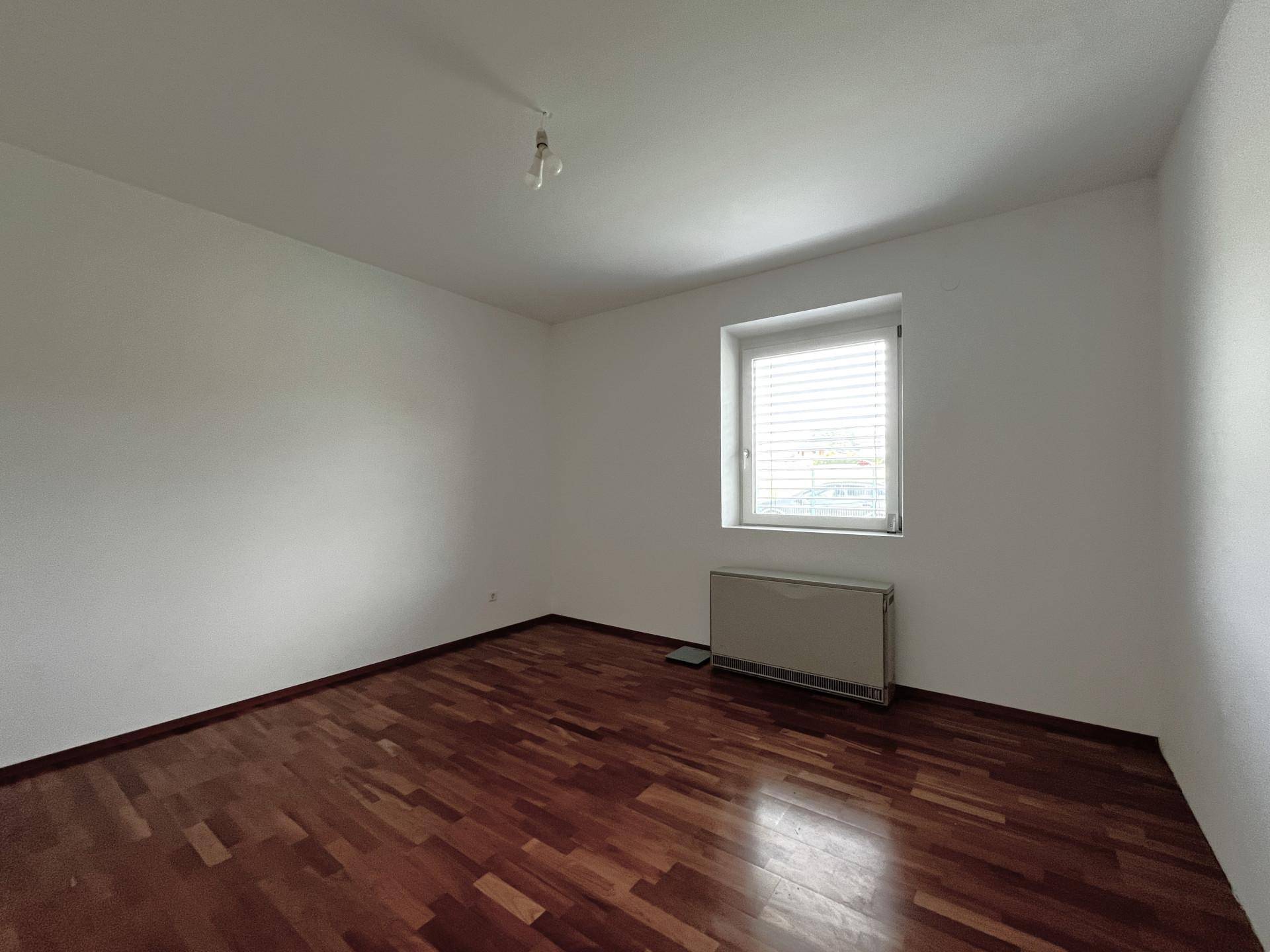 Helles Schlafzimmer mit Holzboden und großem Fenster, ideal für natürliche Belichtung.