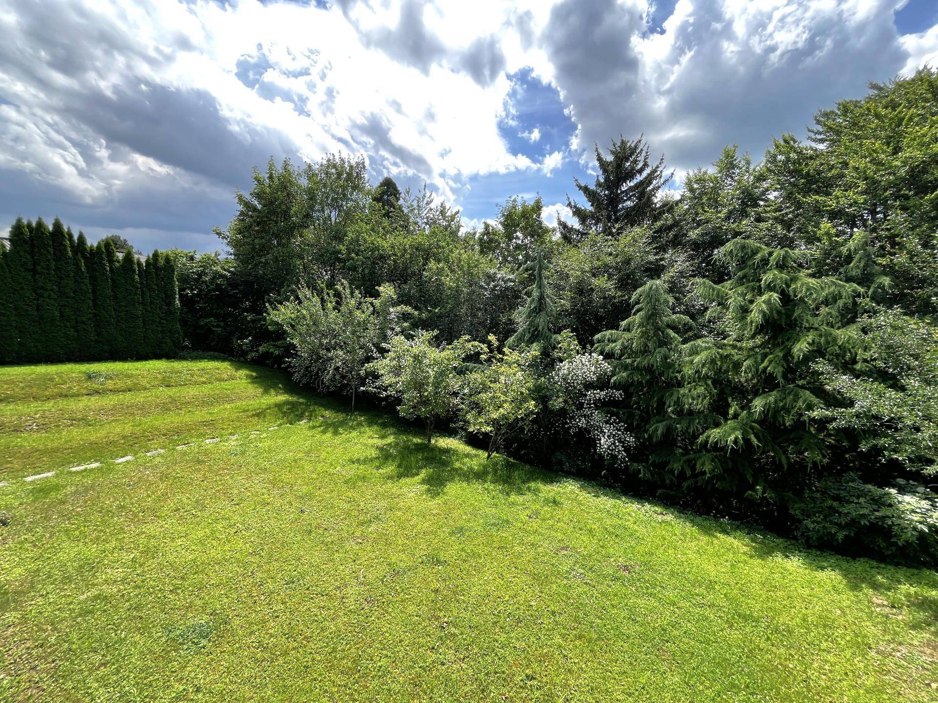 Großer, gepflegter Gartenbereich mit Rasenfläche und üppiger Bepflanzung unter bewölktem Himmel.