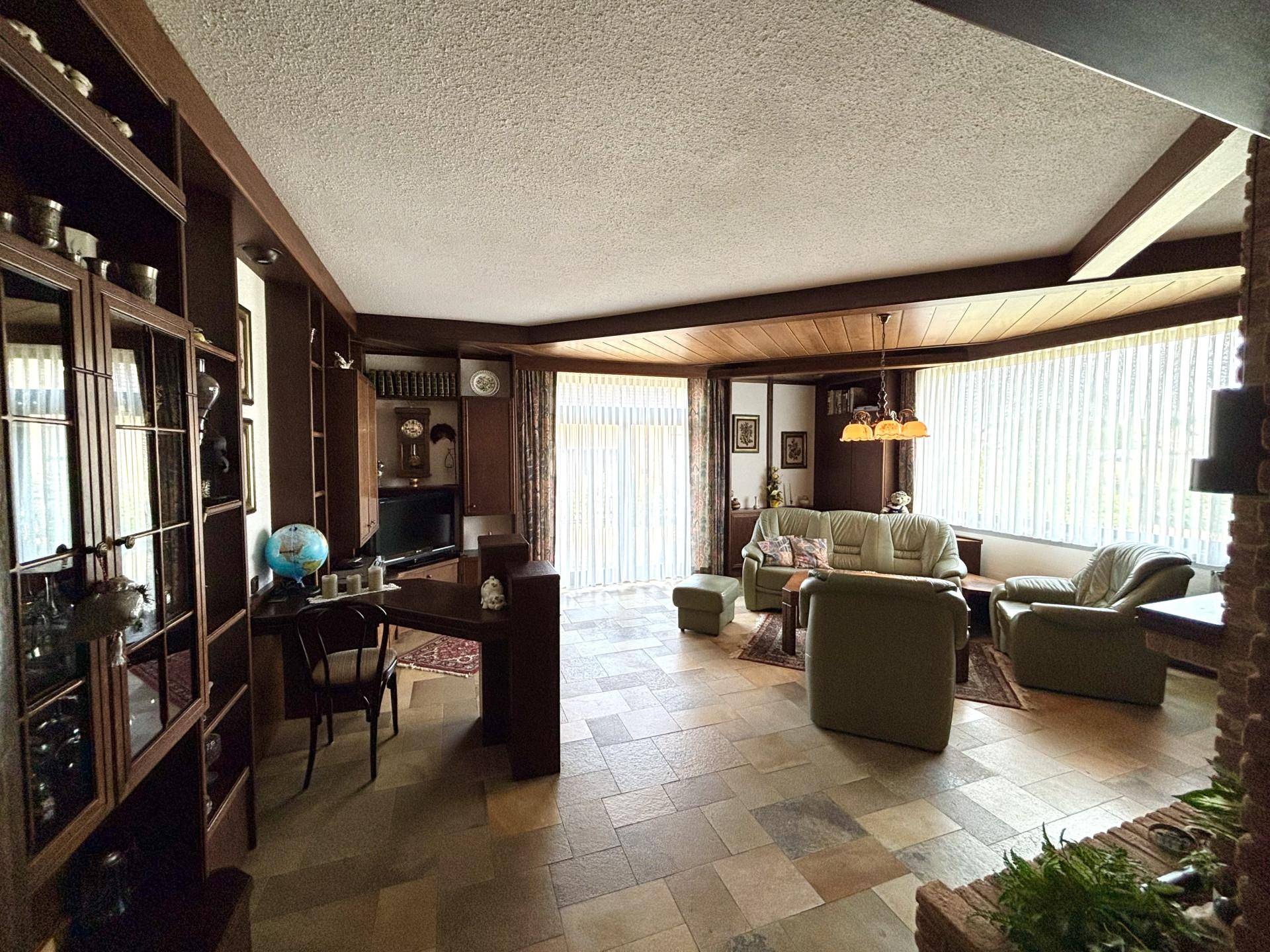 Großzügiges Wohnzimmer mit Fliesenboden, Holzdecken und großen Fenstern.