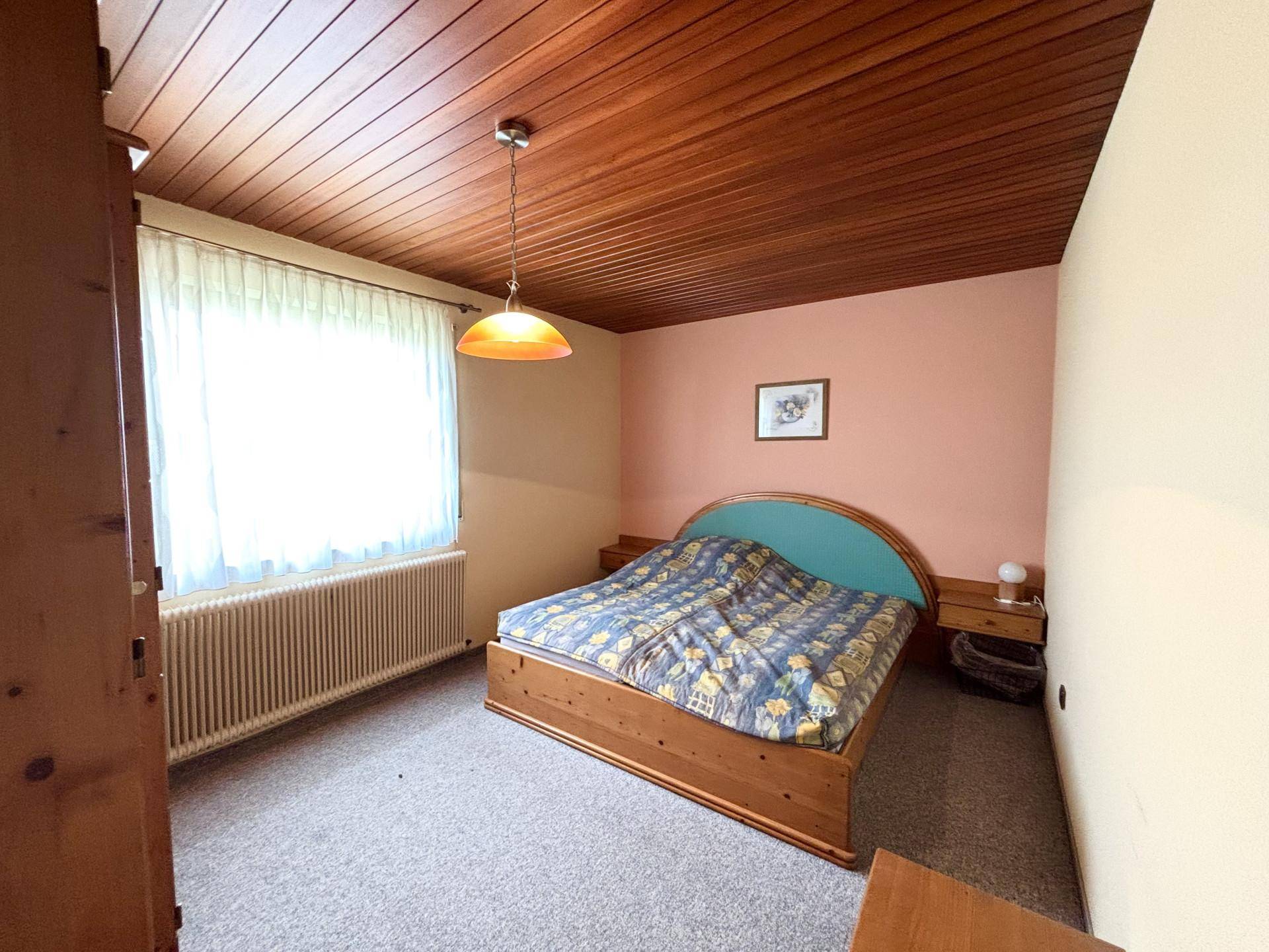 Helles Schlafzimmer mit Teppichboden, Holzdecke und einem Doppelbett.