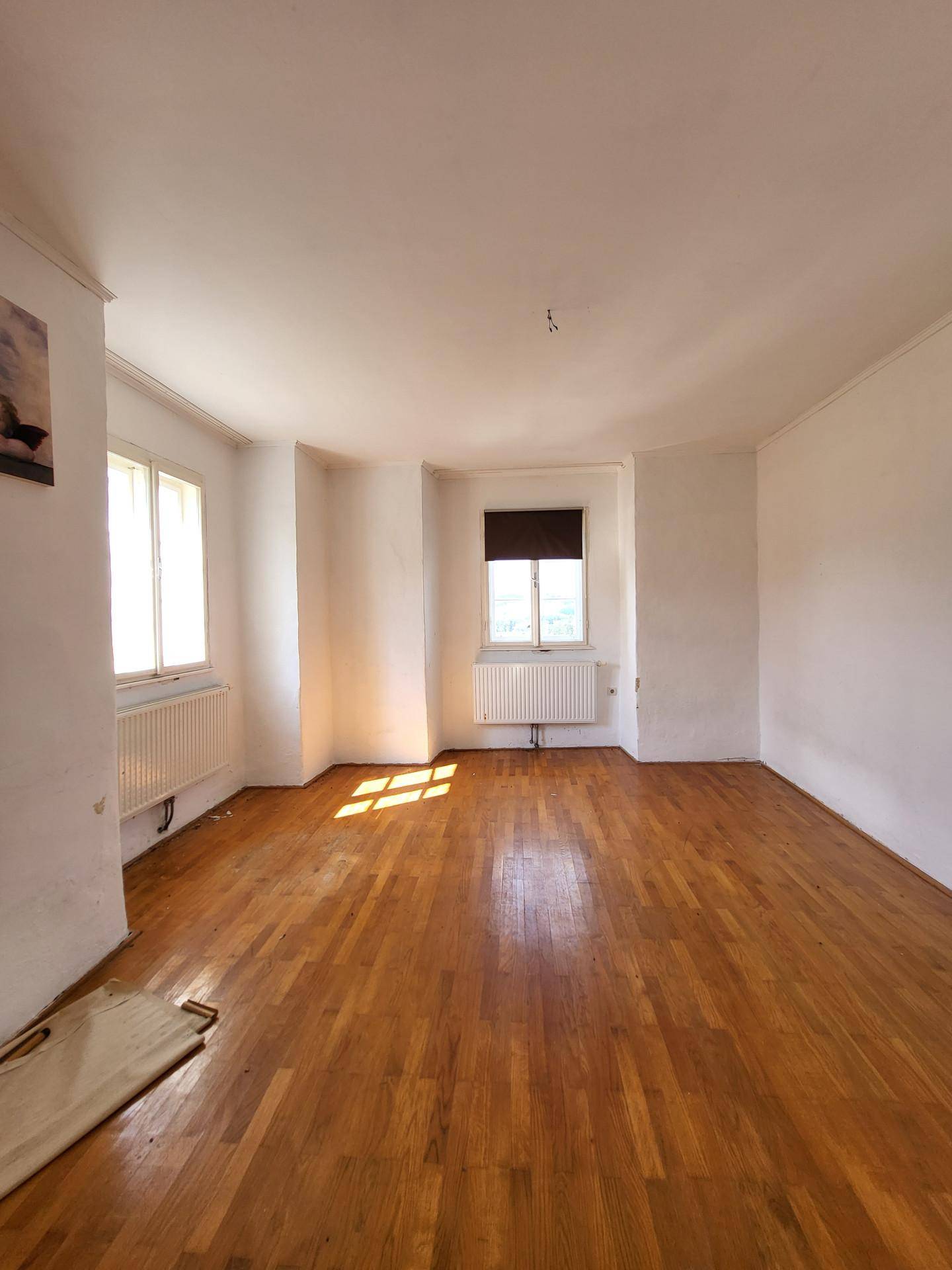 Geräumiges Zimmer mit Holzboden und zwei Fenstern, die viel Tageslicht hereinlassen.