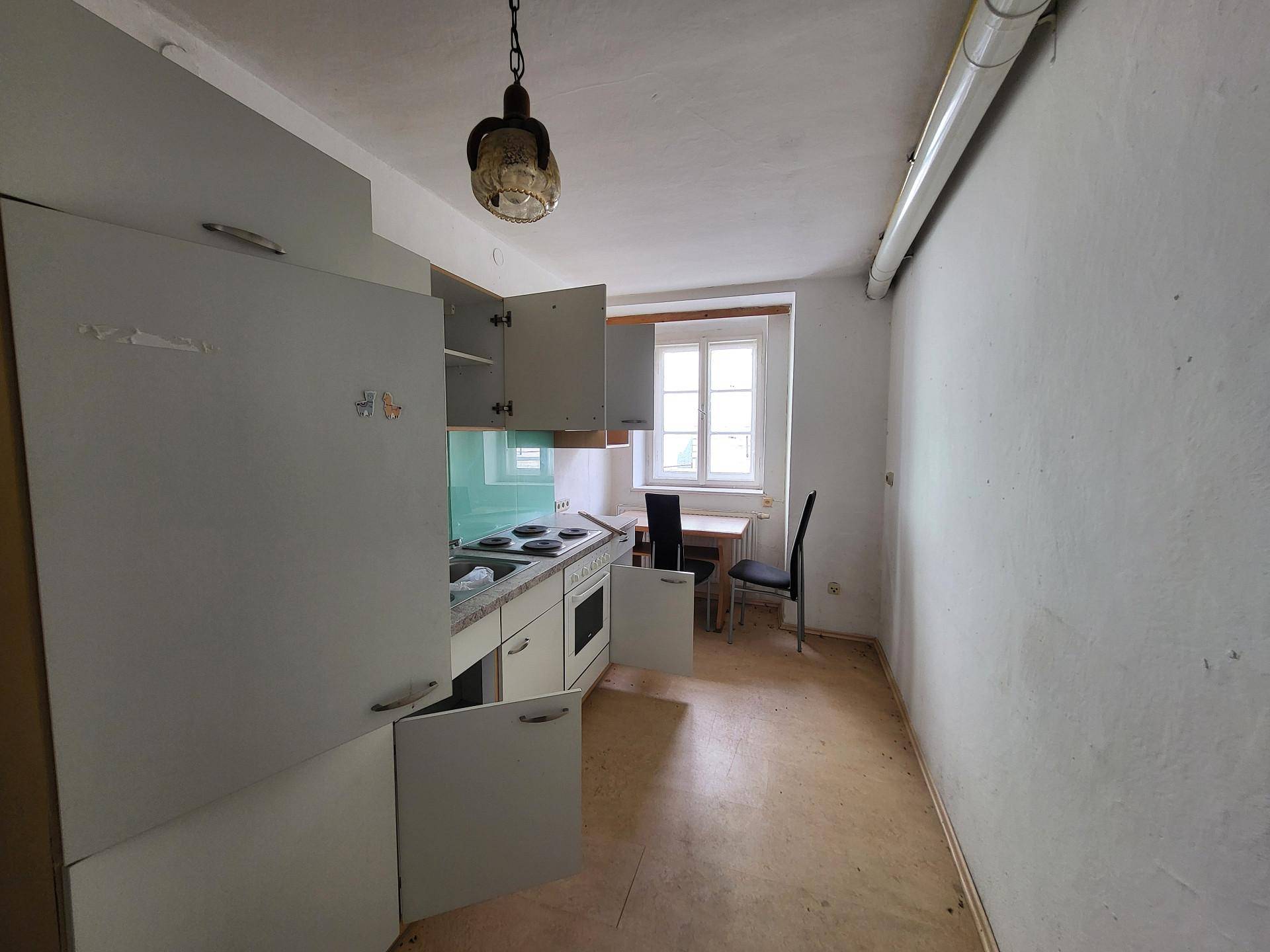 Einfache Küche mit Einbauschränken, Herd und einem kleinen Essbereich am Fenster.