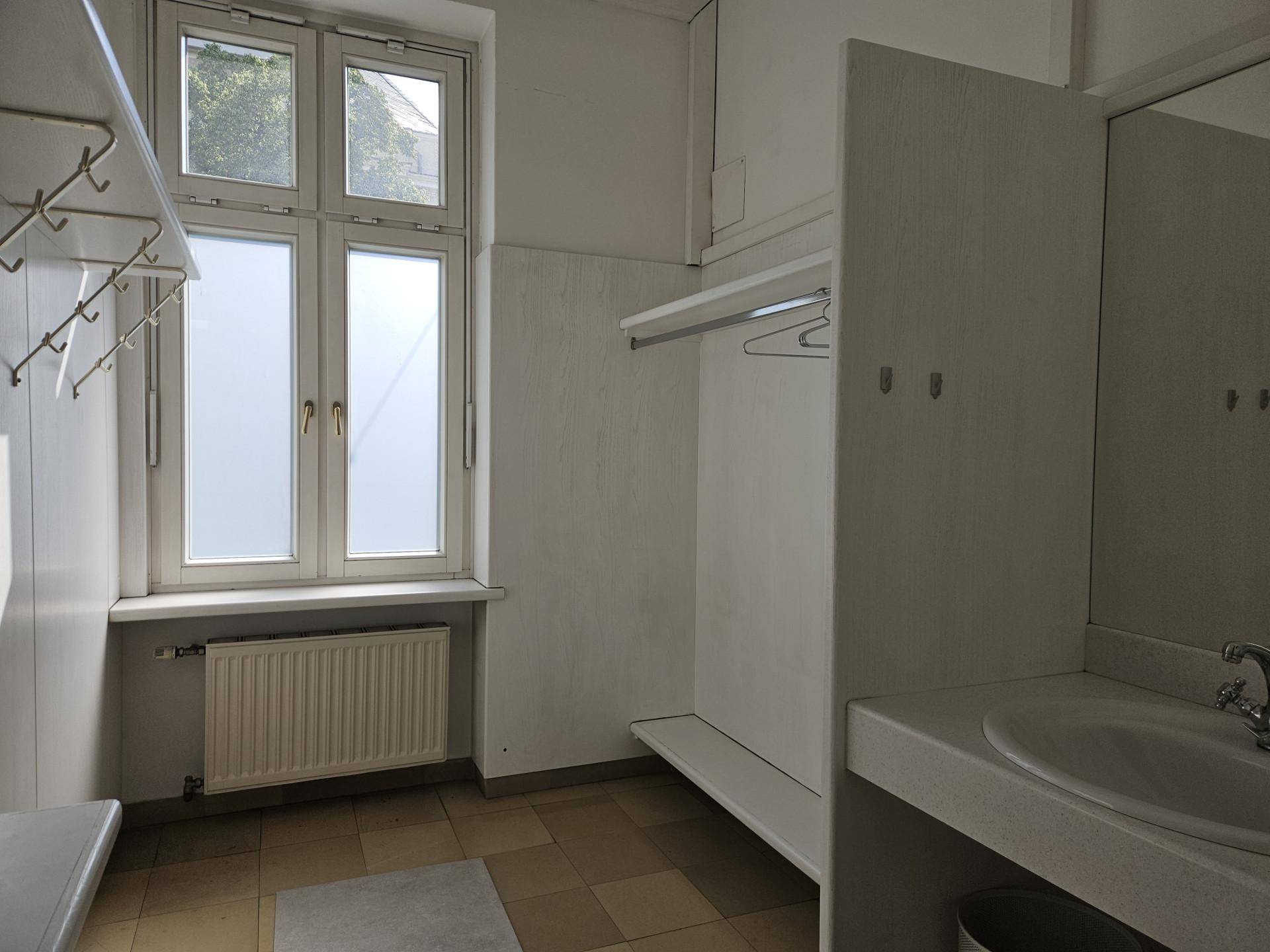 Umkleideraum mit Waschbecken, Spiegel und Kleiderhaken, ausgestattet mit einem Fenster.