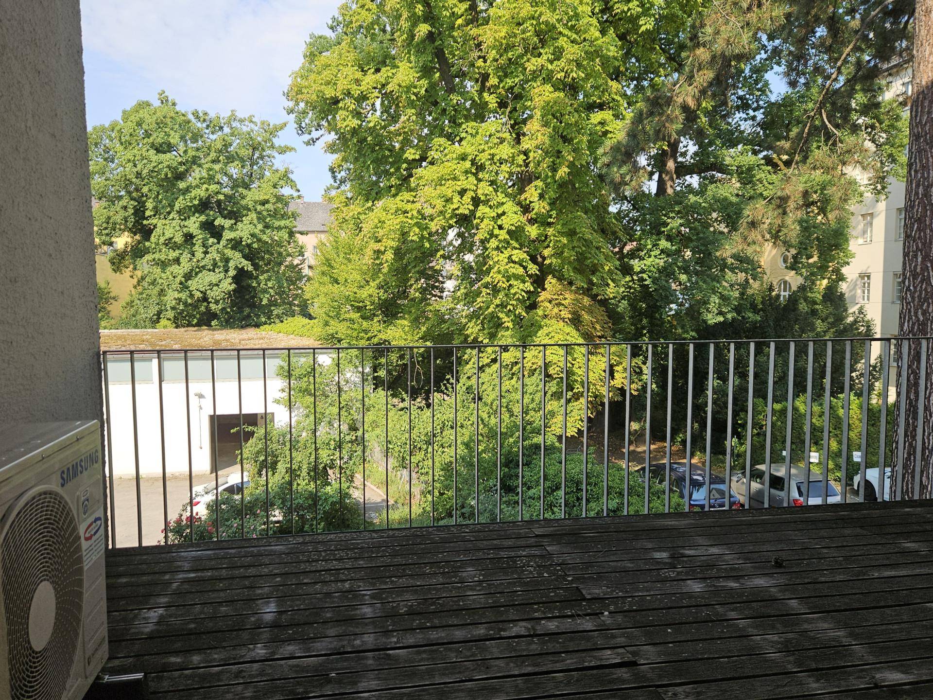 Balkon mit Holzboden und Metallgeländer, bietet einen schönen Blick auf grüne Bäume und die Umgebung.