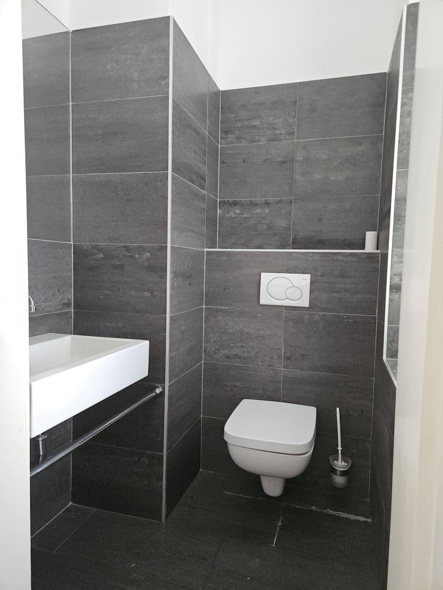 Modernes Gäste-WC mit dunkelgrauen Fliesen, wandhängender Toilette und stilvollem Waschbecken.