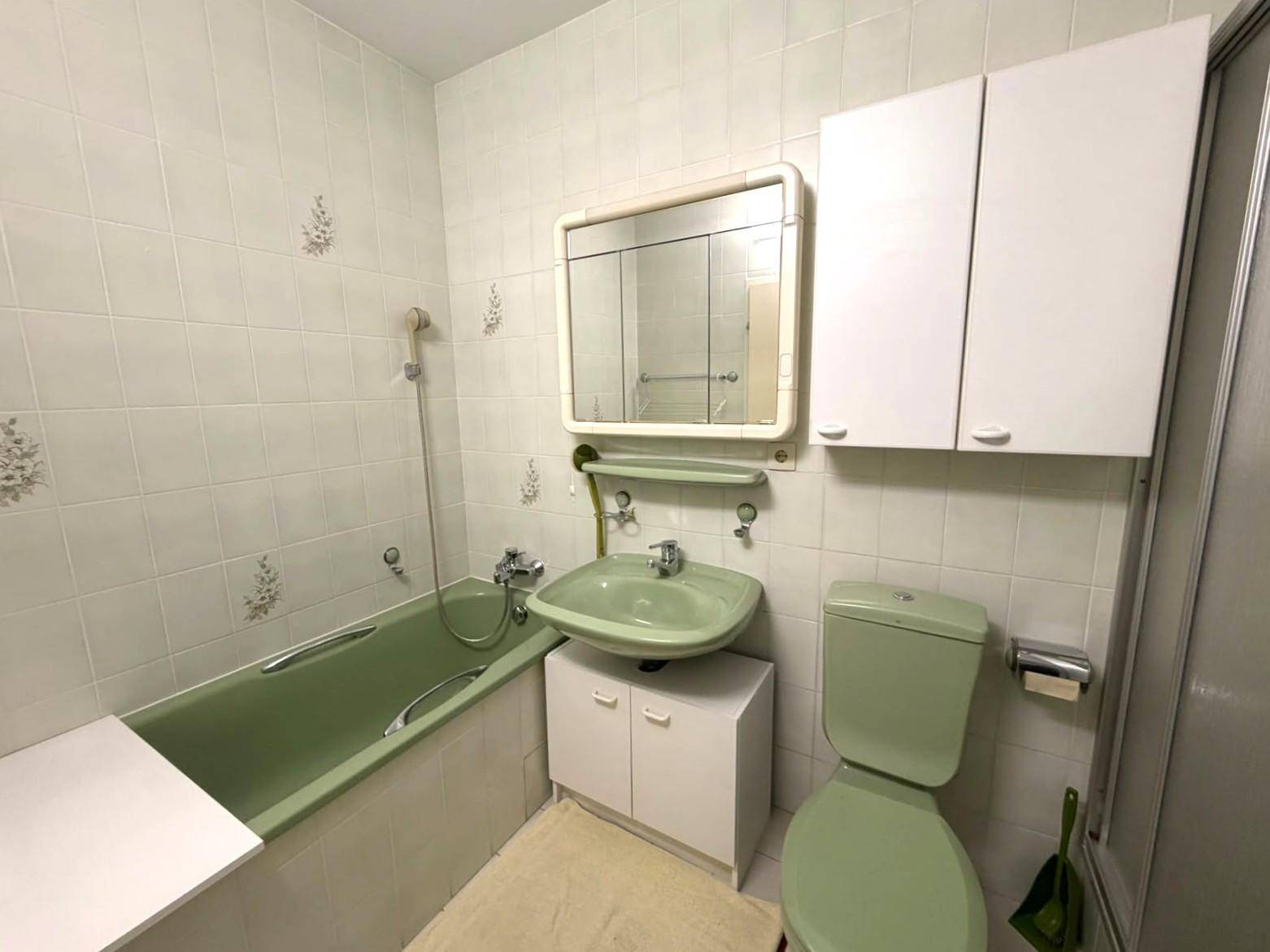Badezimmer im 80er-Jahre-Stil mit grüner Badewanne, Waschbecken und Wandfliesen.