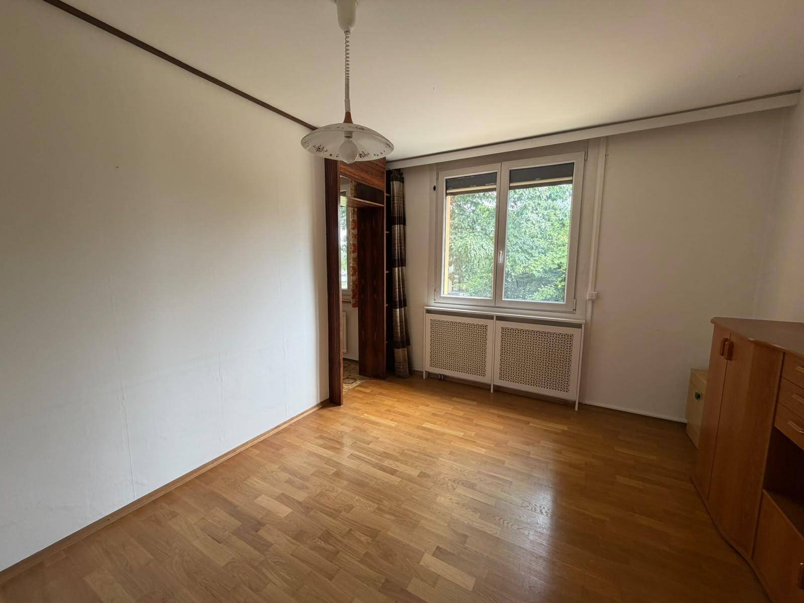 Helles Zimmer mit Parkettboden und Fenster mit Blick auf Bäume.