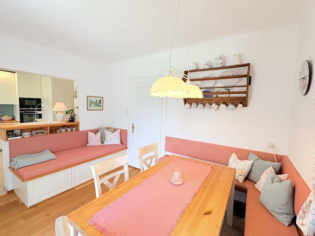 Heller Essbereich mit Holztisch und gemütlichen Sitzbänken, offen zur angrenzenden Küche.