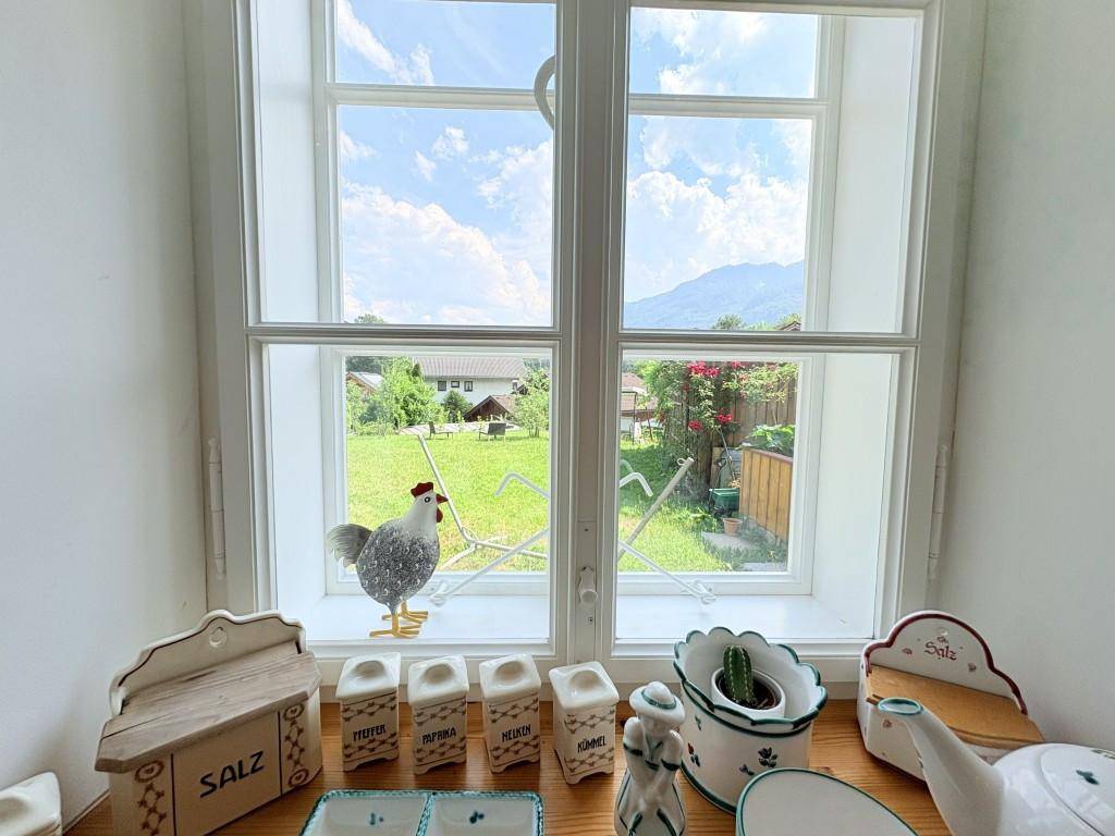 Fenster mit Blick auf den grünen Garten und die umliegende Berglandschaft, dekoriert mit traditionellen Elementen.