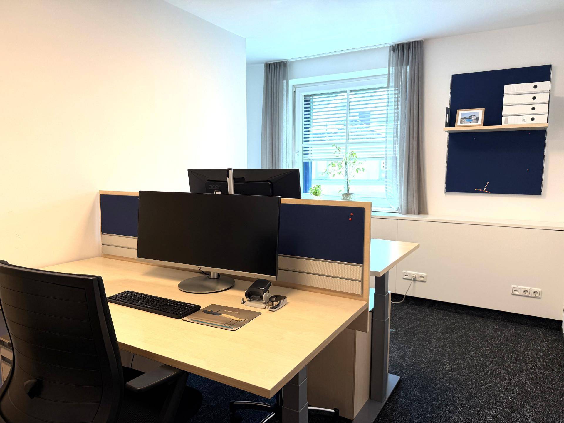 Moderner Büroraum mit Schreibtisch, Computerbildschirmen und Teppichboden.