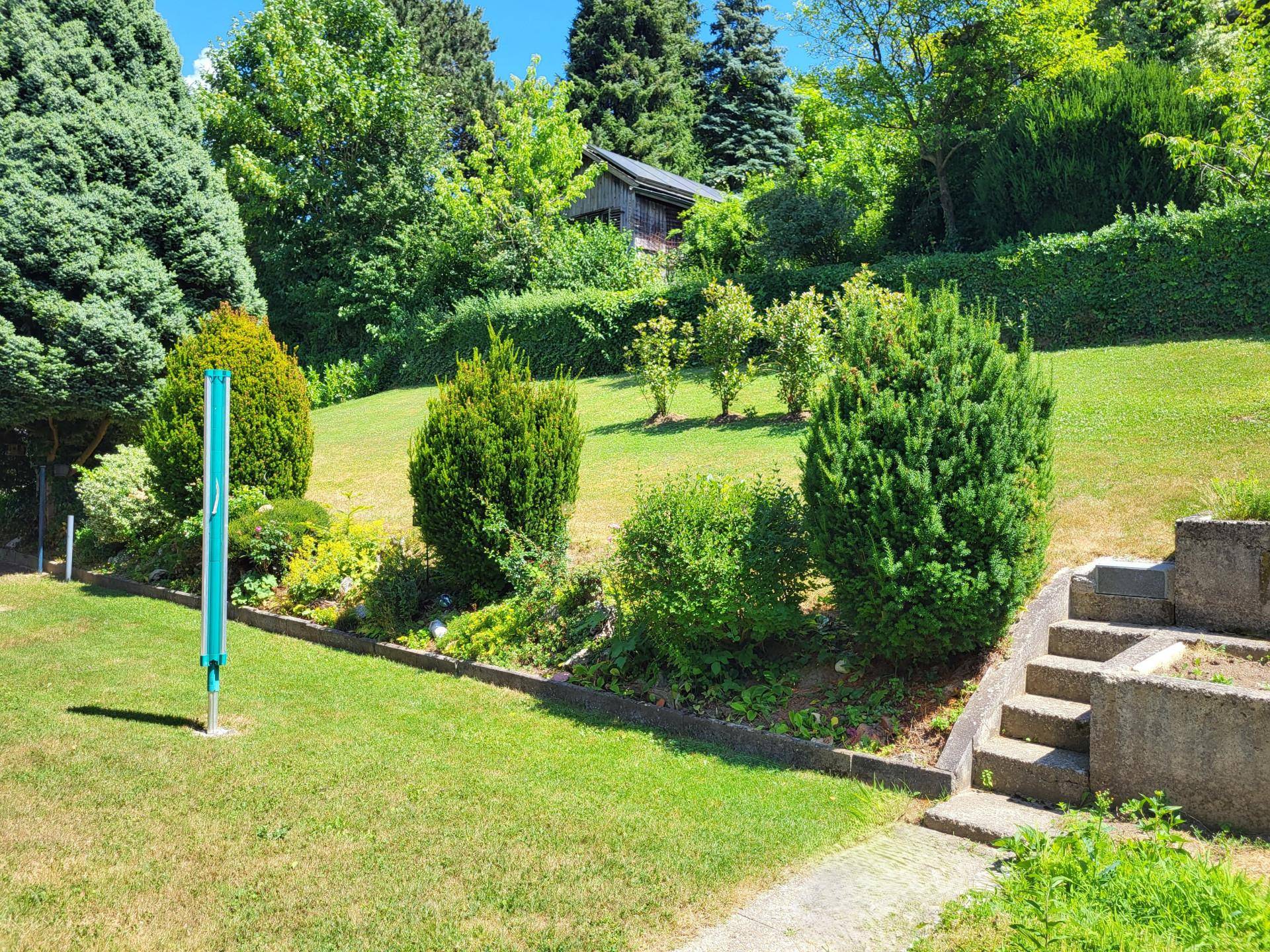 Hanglage des Gartens mit Stufen, üppiger Bepflanzung und einem kleinen Gartenhaus im Hintergrund.