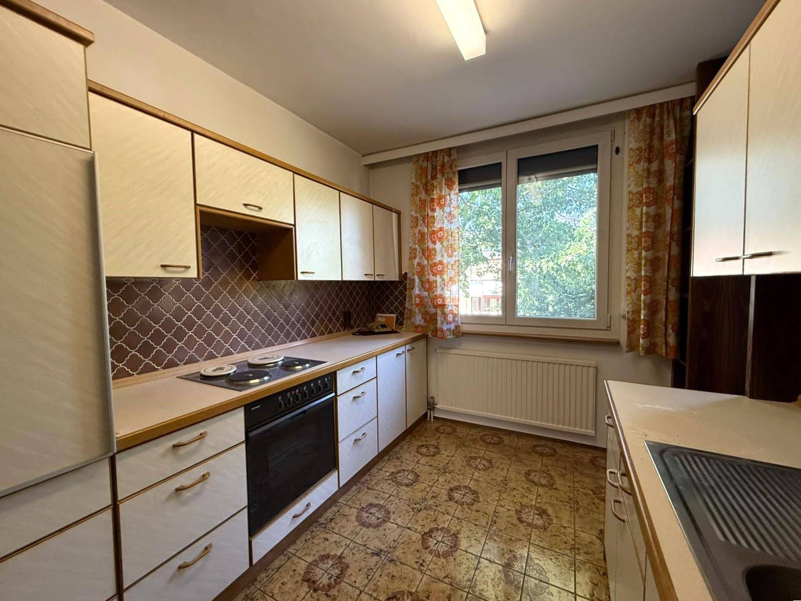 Küche im 80er-Jahre-Stil mit Einbaugeräten, Fliesenboden und Fenster.