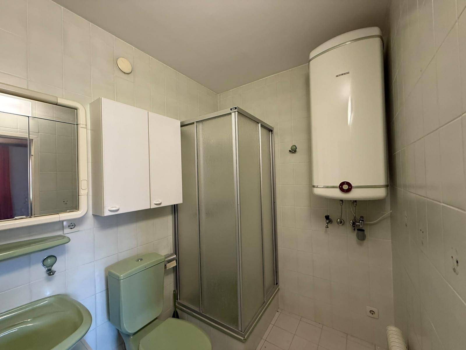 Badezimmer mit Duschkabine, WC, Waschbecken und Warmwasserboiler.