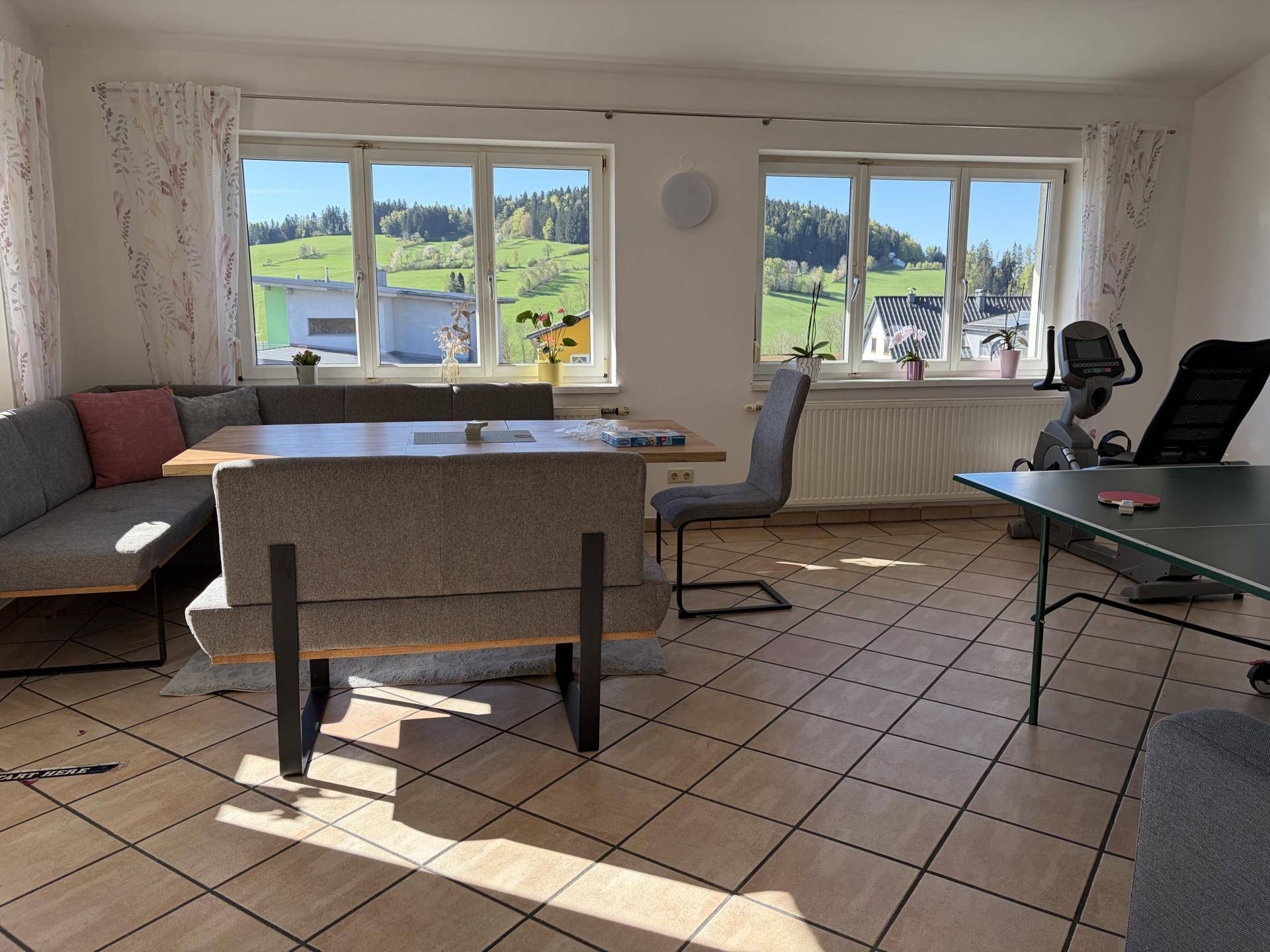 Geräumiger Essbereich mit Fliesenboden, großen Fenstern und Blick auf die grüne Umgebung.