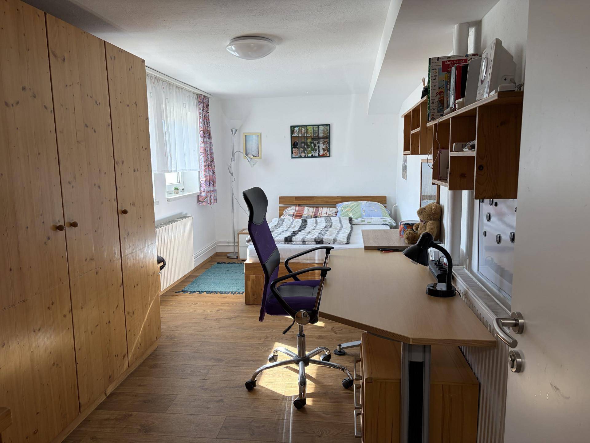Geräumiges Schlafzimmer mit großem Holzschrank, Schreibtisch und Fenster.