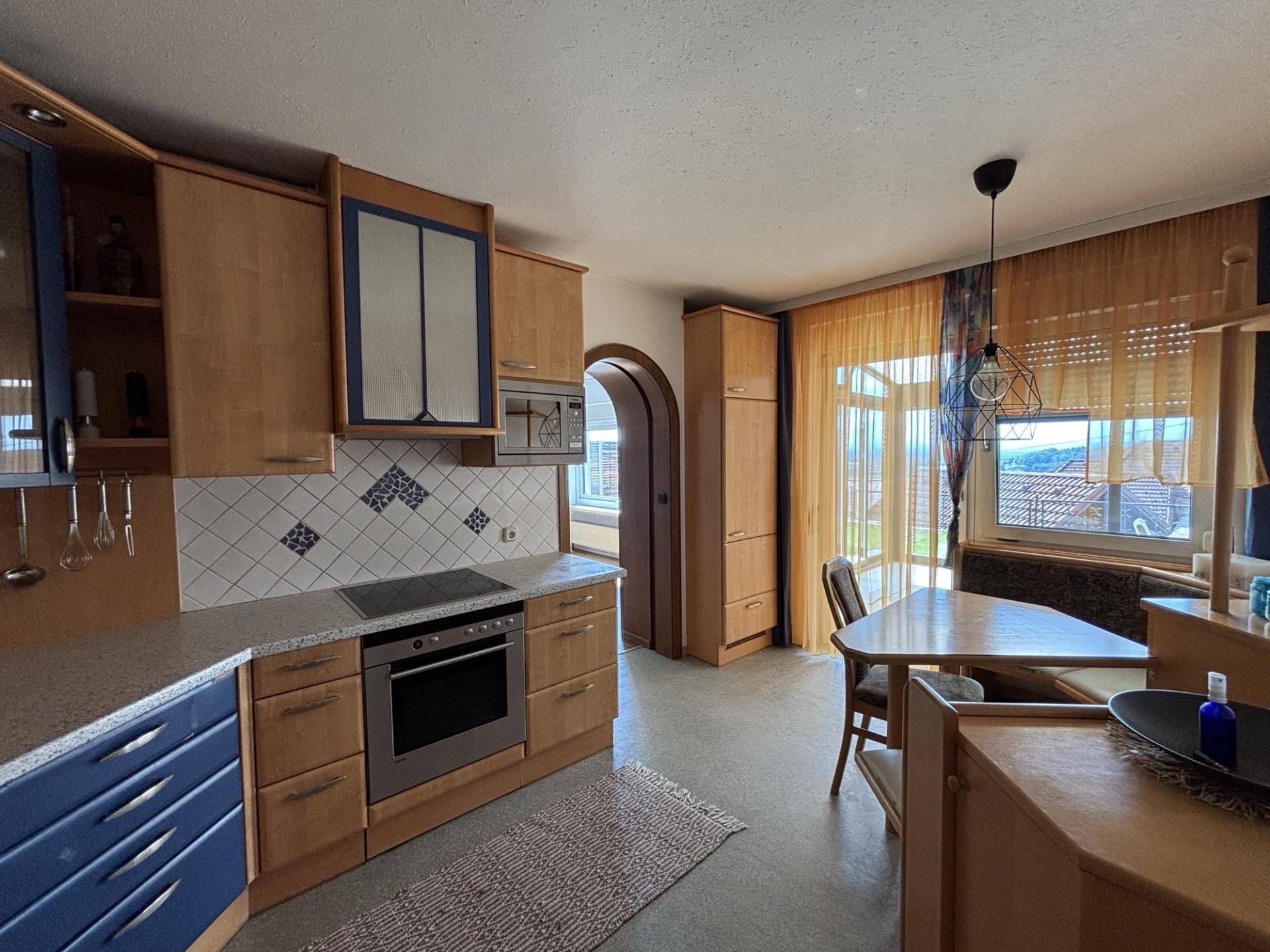 Funktionale Küche mit Holzschränken, Essbereich und Blick auf die umliegende Landschaft.