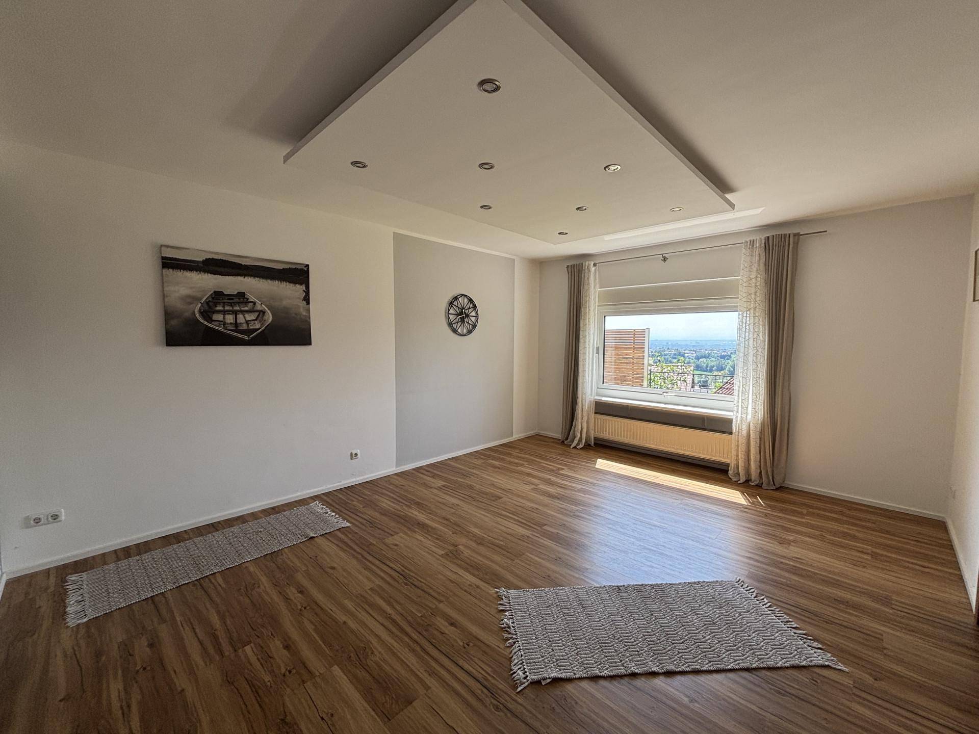 Helles Wohnzimmer mit modernem Deckenlicht, Holzoptikboden und weitem Ausblick.