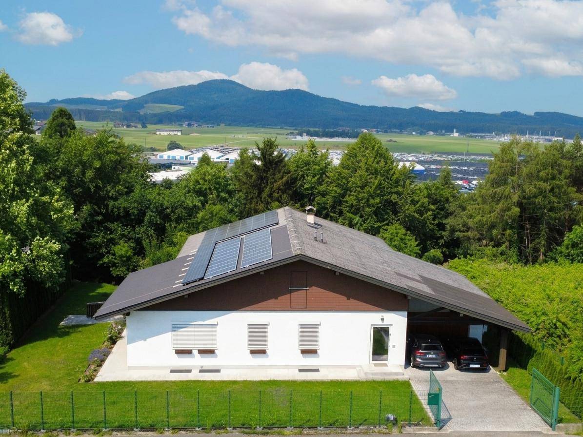 Einfamilienhaus mit Photovoltaikanlage auf dem Dach, Carport und Bergblick im Hintergrund.