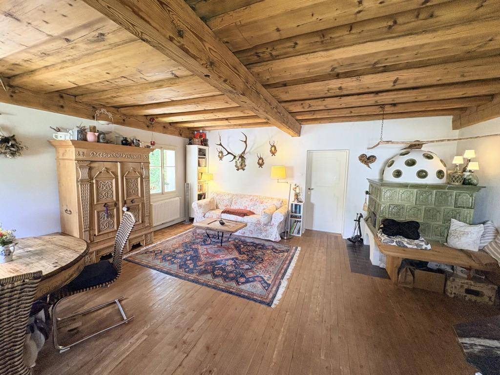 Rustikales Wohnzimmer mit Holzbalkendecke, Kachelofen und traditionellen Möbeln.