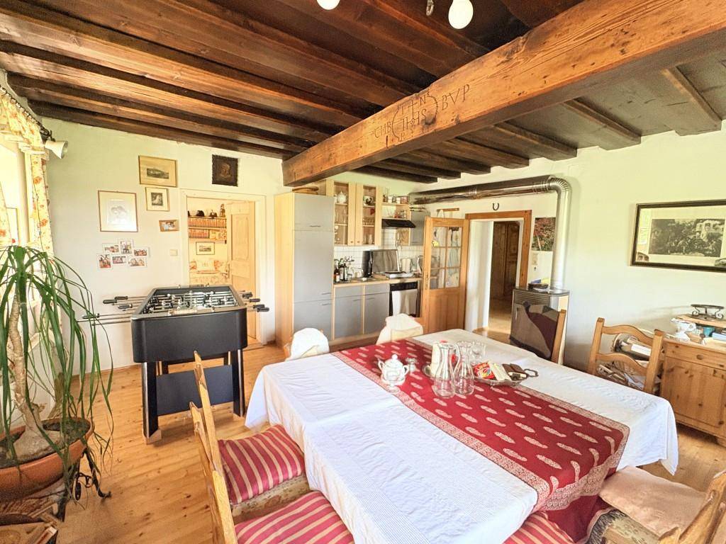 Geräumiger Essbereich mit Holzbalkendecke, großem Esstisch und Blick in die Küche.