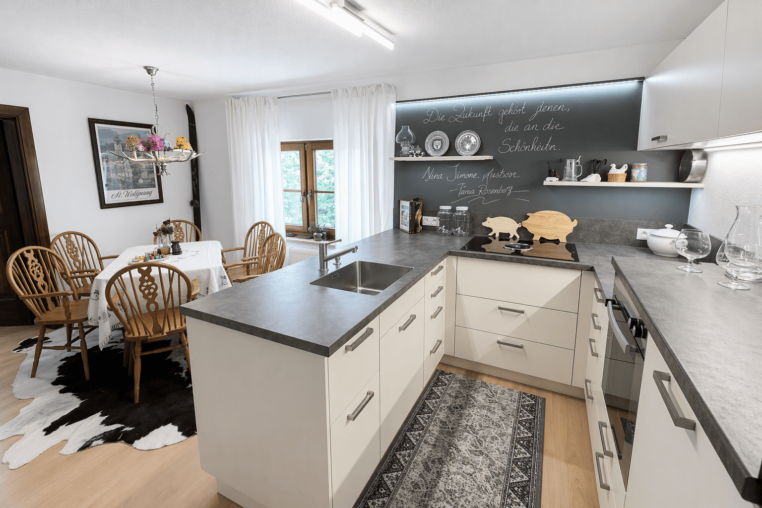 Moderne Küche mit grauen Arbeitsplatten, weißen Schränken und Essbereich im Landhausstil.
