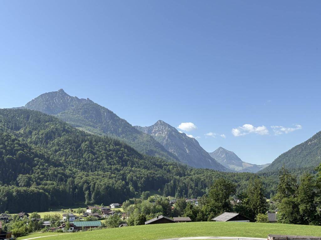 Panoramablick auf eine grüne Berglandschaft mit einem Dorf im Tal.