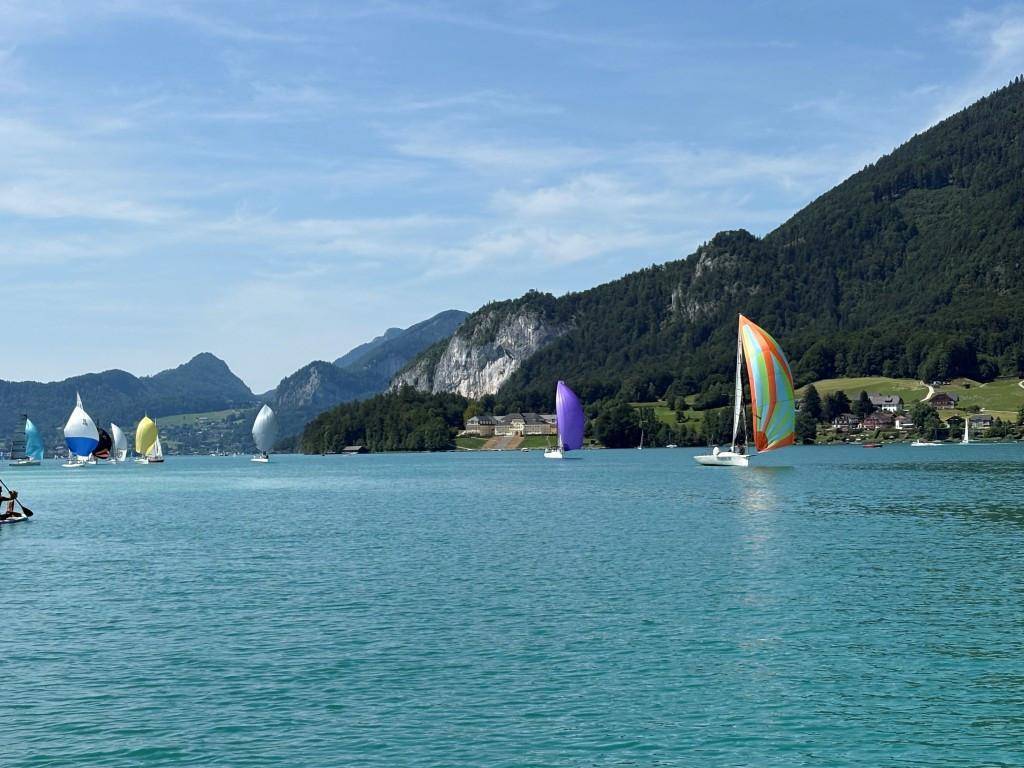 Segelboote auf einem klaren Bergsee, umgeben von grünen Hügeln und Bergen.