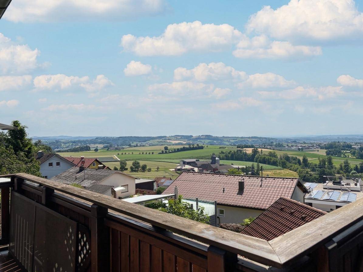 Weitläufiger Blick vom Balkon über eine grüne Hügellandschaft mit vereinzelten Häusern.