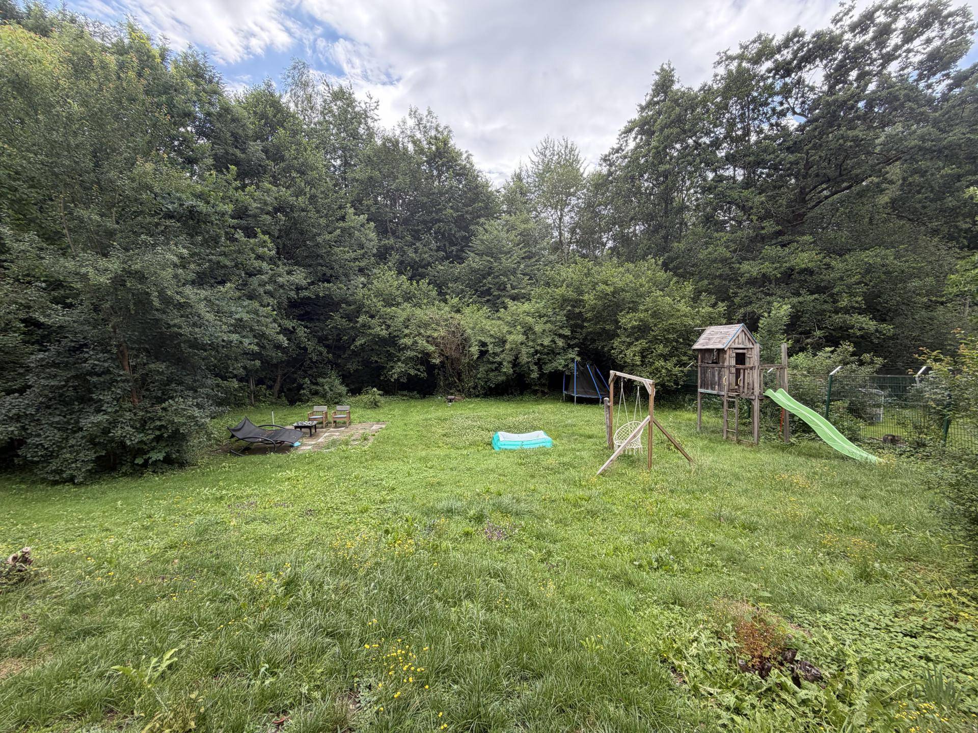 Großer Garten mit Rasenfläche, Spielplatz für Kinder und umgeben von Bäumen.