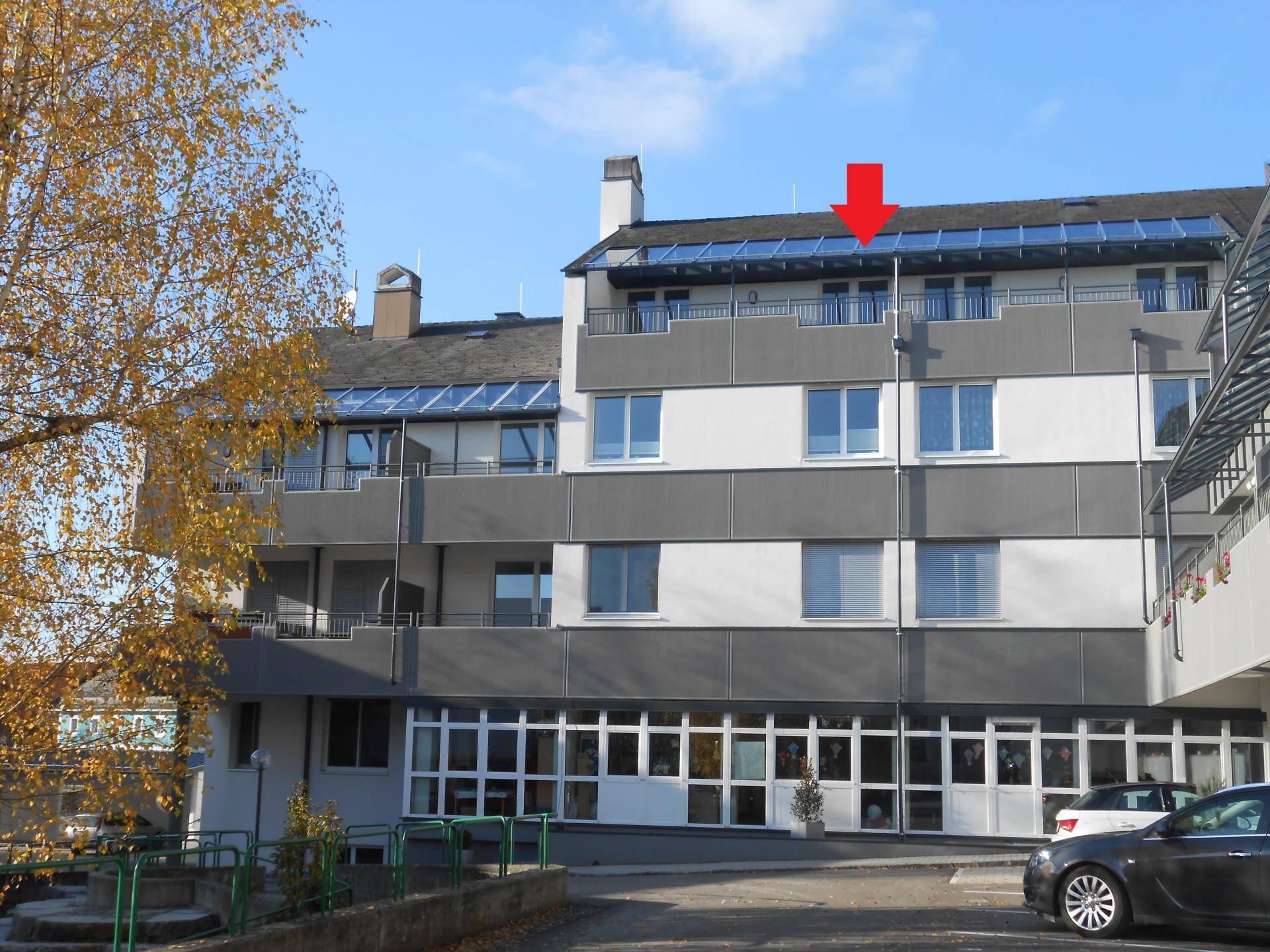 Mehrstöckiges Gebäude mit moderner Fassade, Balkonen und Glasdachkonstruktion im oberen Bereich.