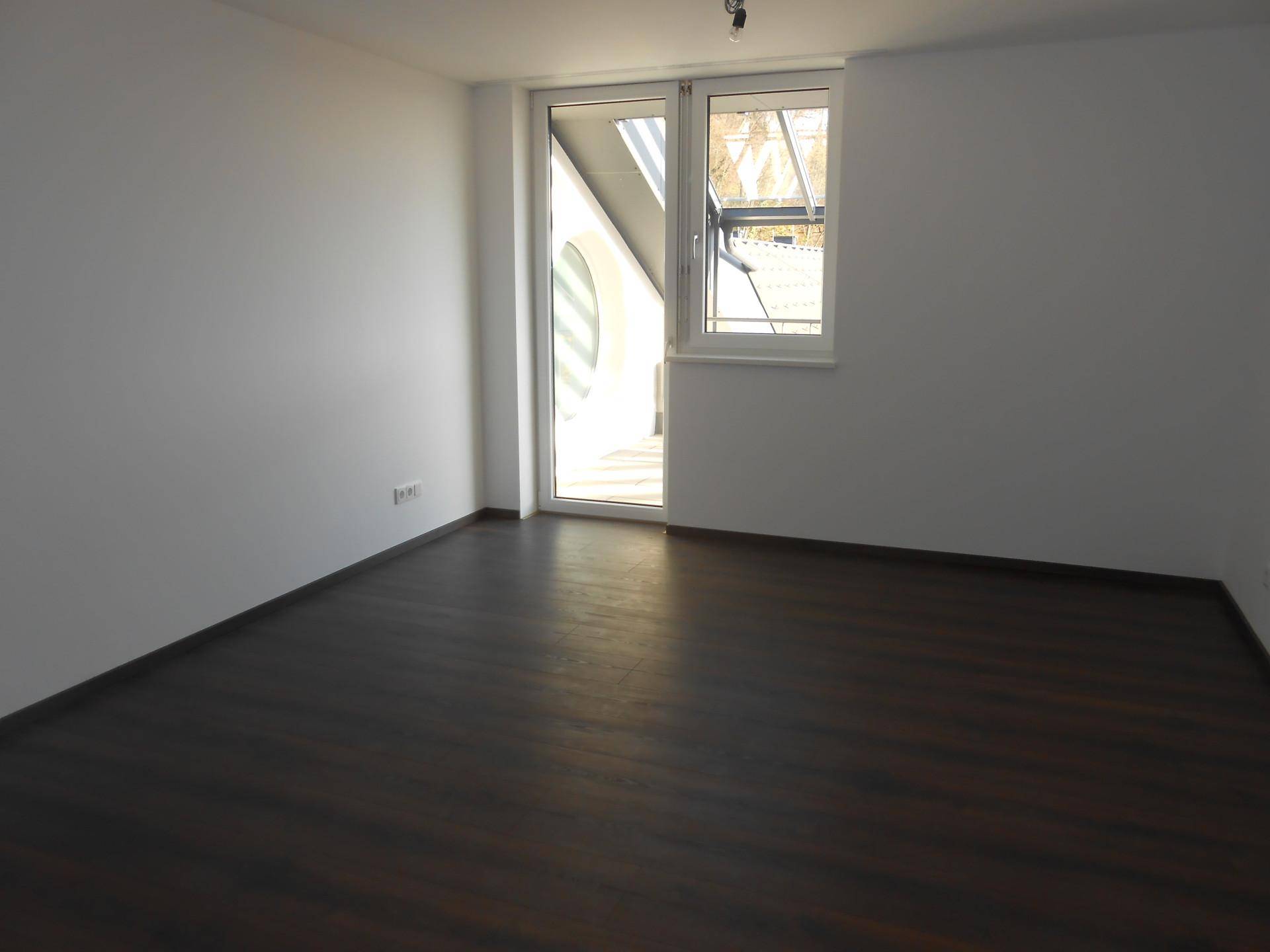 Leerer Raum mit dunklem Holzboden, weißen Wänden und Zugang zu einer überdachten Terrasse.