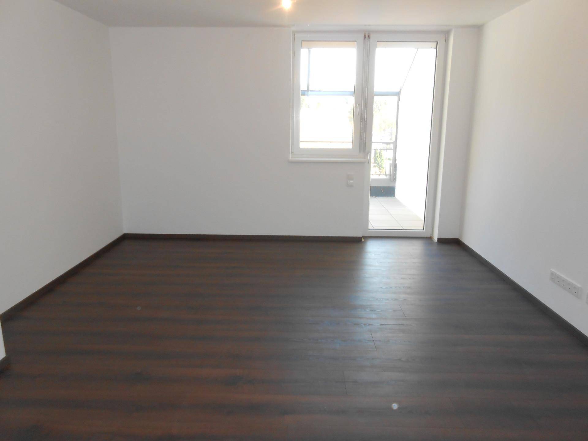 Heller, leerer Raum mit dunklem Holzboden, weißen Wänden und Zugang zu einem Außenbereich.