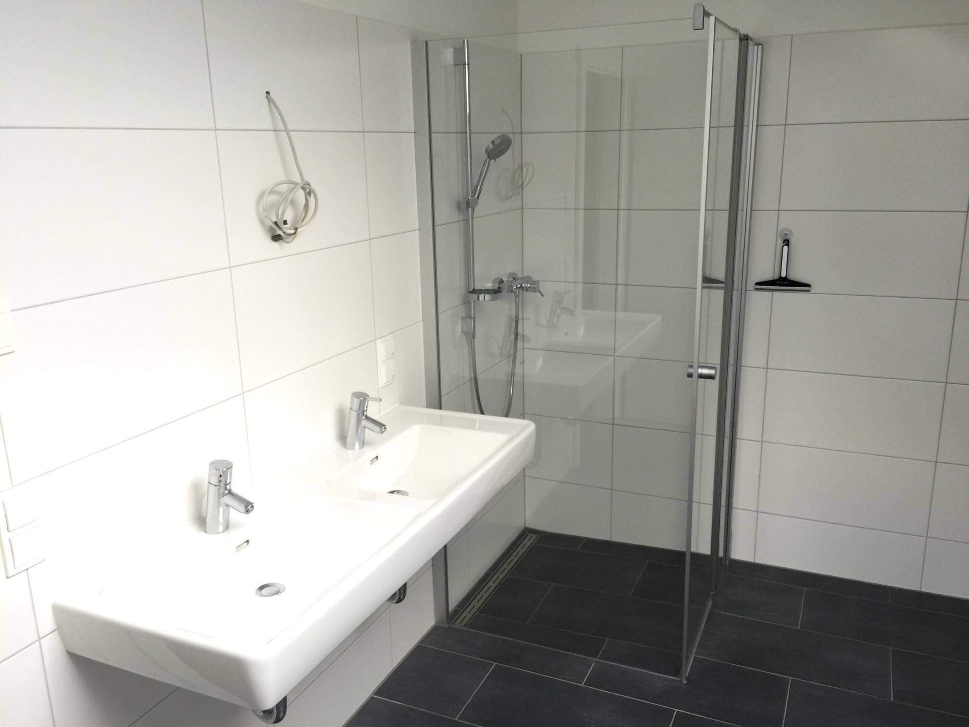 Modernes Badezimmer mit Doppelwaschbecken, begehbarer Dusche und weißen Wand- und dunklen Bodenfliesen.