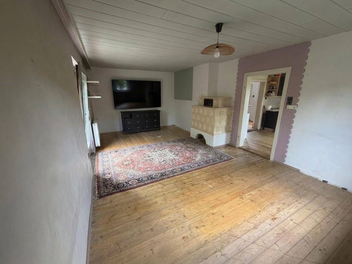 Gemütliches Wohnzimmer mit Holzdielenboden, traditionellem Kachelofen und Teppich.