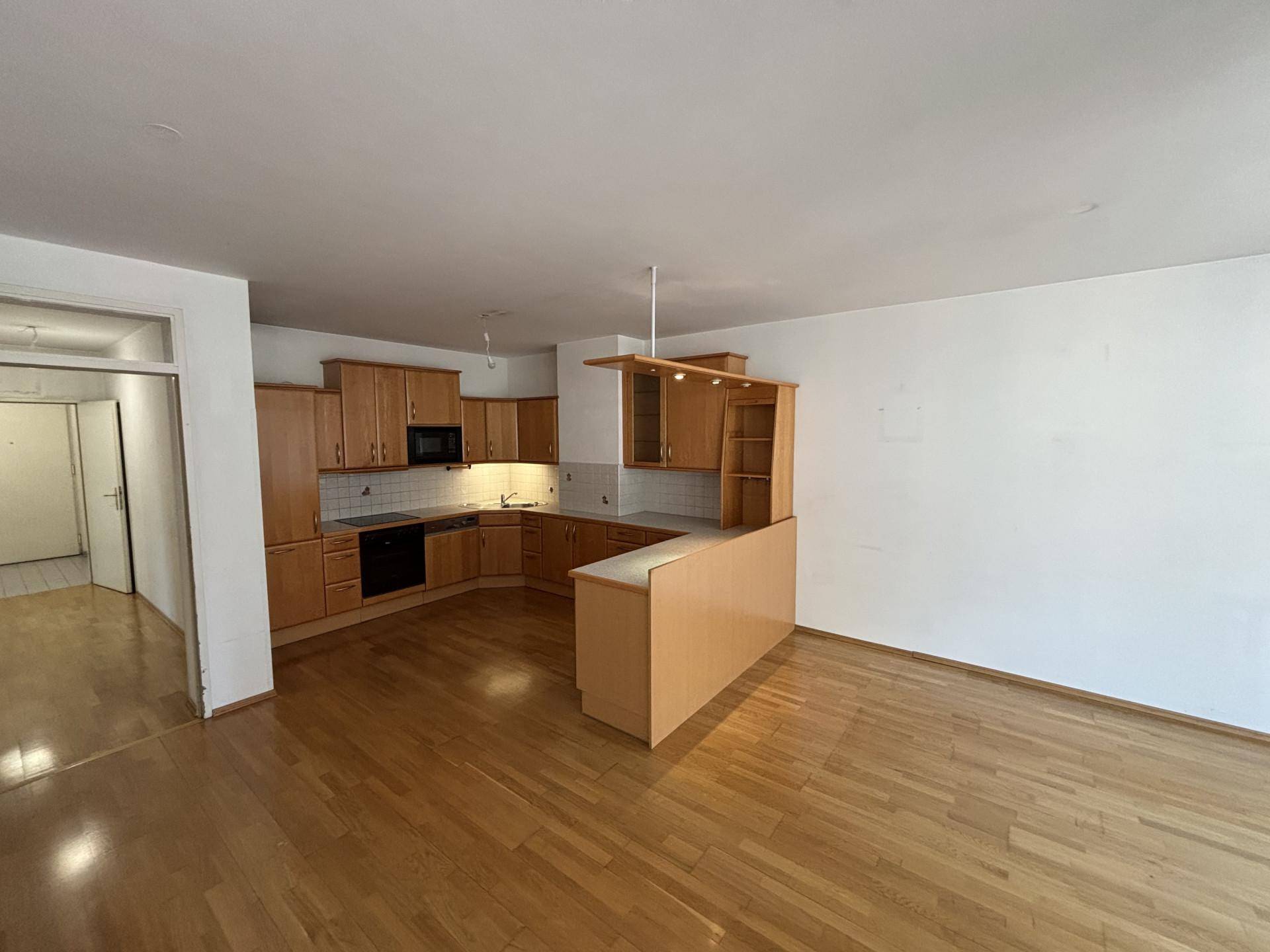 Offene Küche mit hellen Holzschränken, integrierten Geräten und einer Frühstücksbar, verbunden mit einem Wohnbereich.