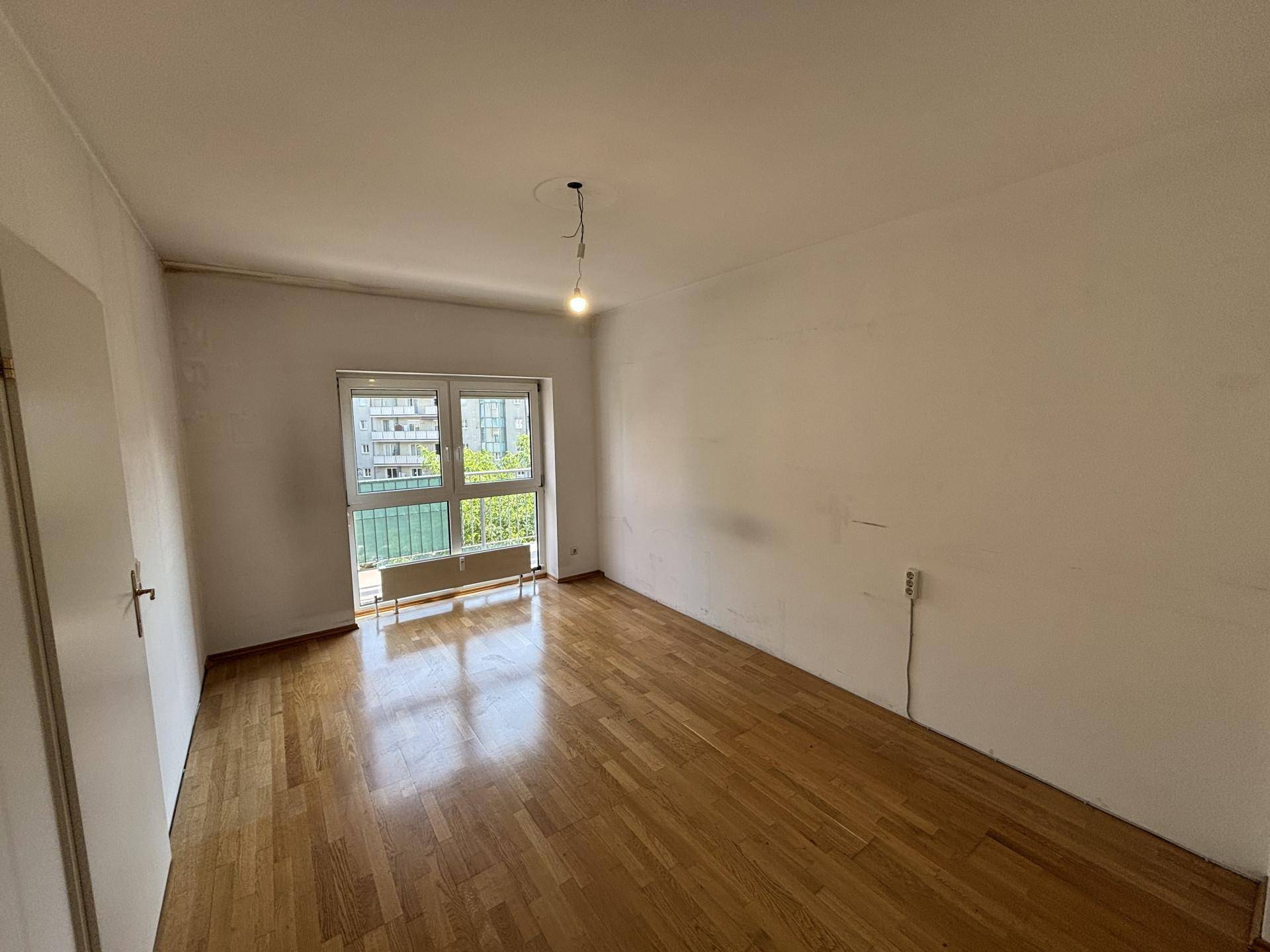 Helles Zimmer mit Holzboden und einem Fenster, das einen angenehmen Blick ins Grüne bietet.