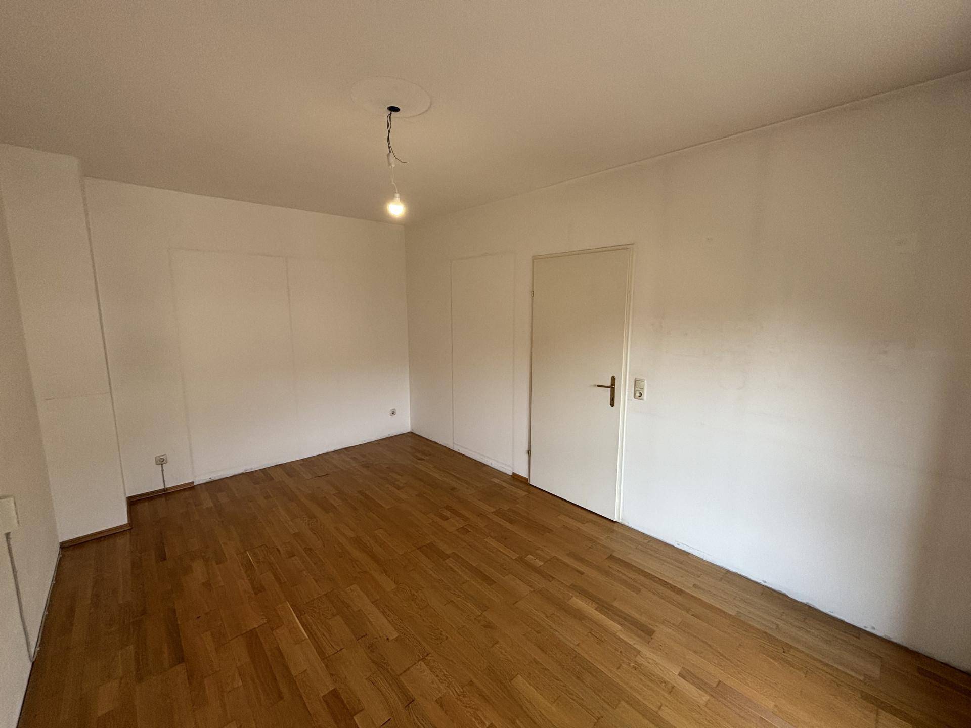 Schlichtes Zimmer mit Holzboden und weißen Wänden, ideal als Schlafzimmer oder Arbeitszimmer nutzbar.
