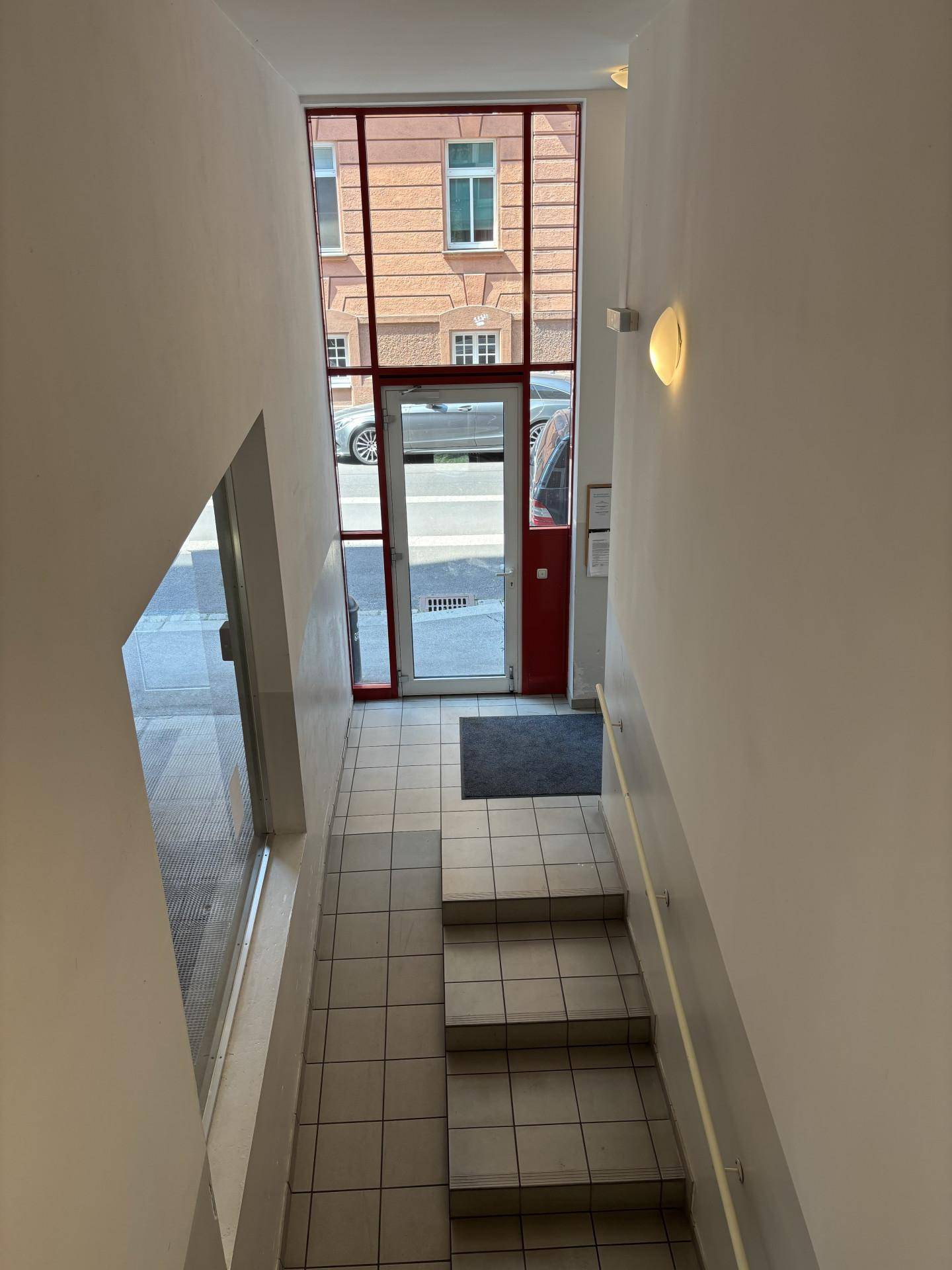 Treppenhaus und Eingangsbereich mit Fliesenboden und einer Glastür, die zur Straße führt.