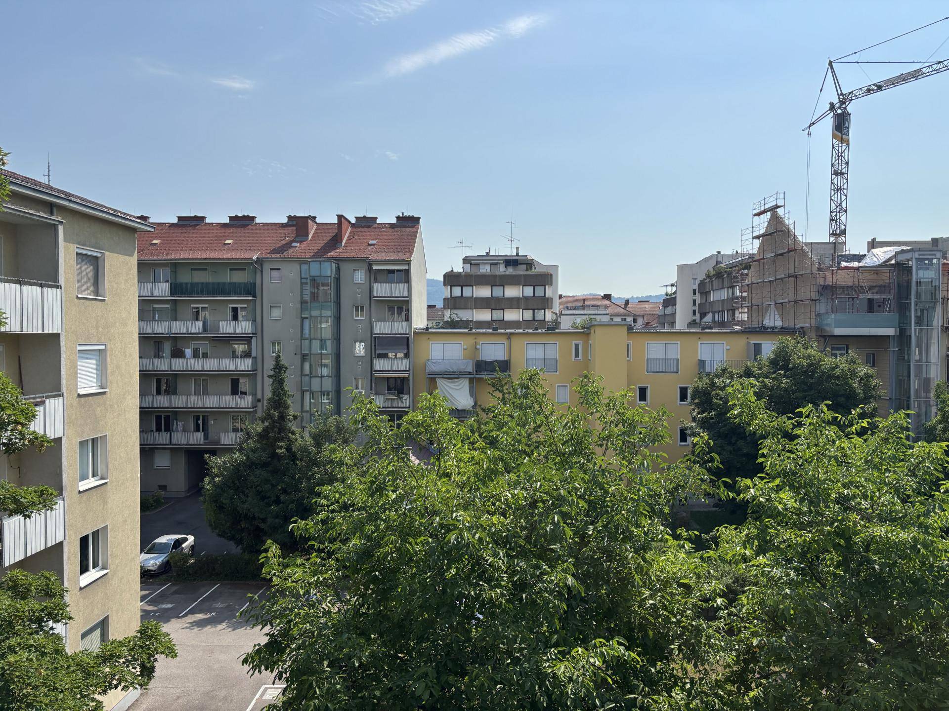 Panoramablick auf mehrere Wohngebäude und Bäume, mit einem Baukran im Hintergrund unter blauem Himmel.