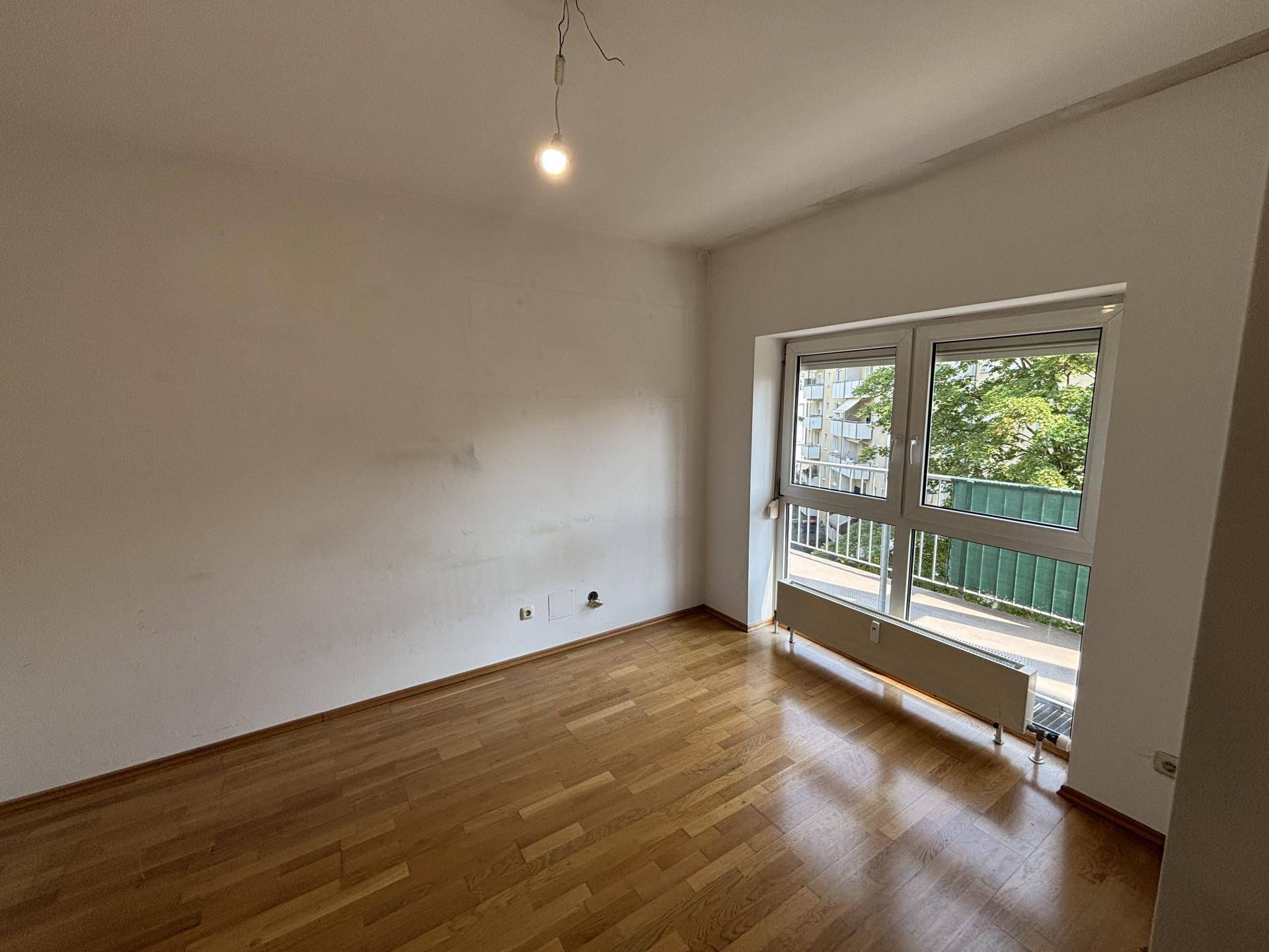 Helles Zimmer mit Holzboden und einem Fenster, das einen erfrischenden Blick ins Grüne bietet.