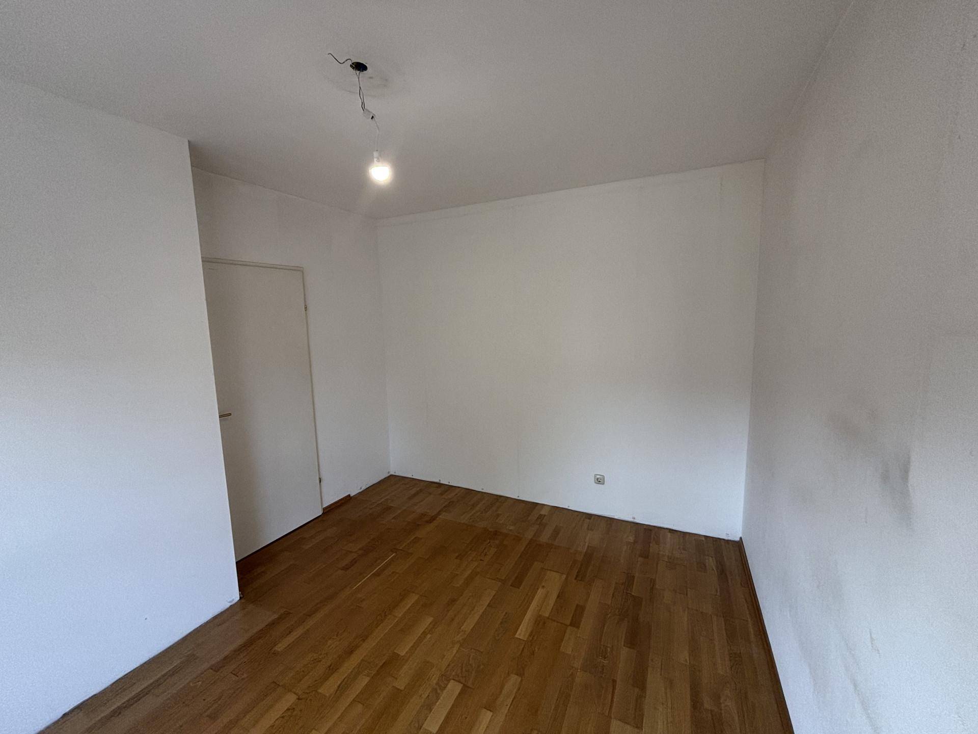 Schlichtes Zimmer mit Holzboden und weißen Wänden, vielseitig nutzbar als Schlaf- oder Arbeitszimmer.