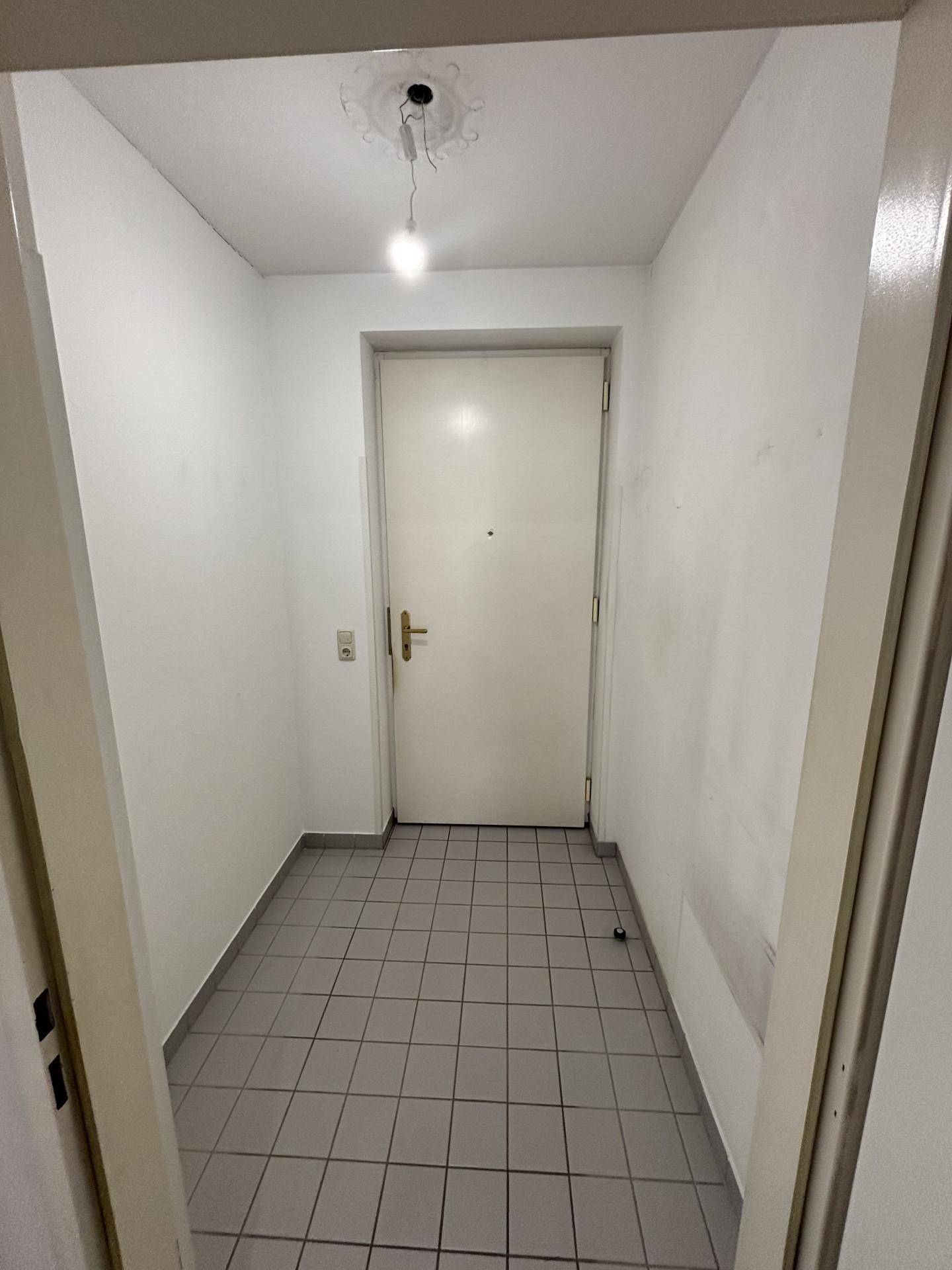 Eingangsbereich mit Fliesenboden und einer weißen Haustür, die in die Wohnung führt.