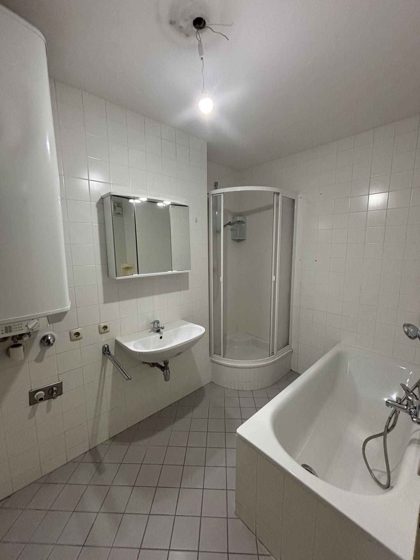 Badezimmer mit weißen Wandfliesen, grauen Bodenfliesen, Badewanne, Waschbecken und einer Eckdusche.