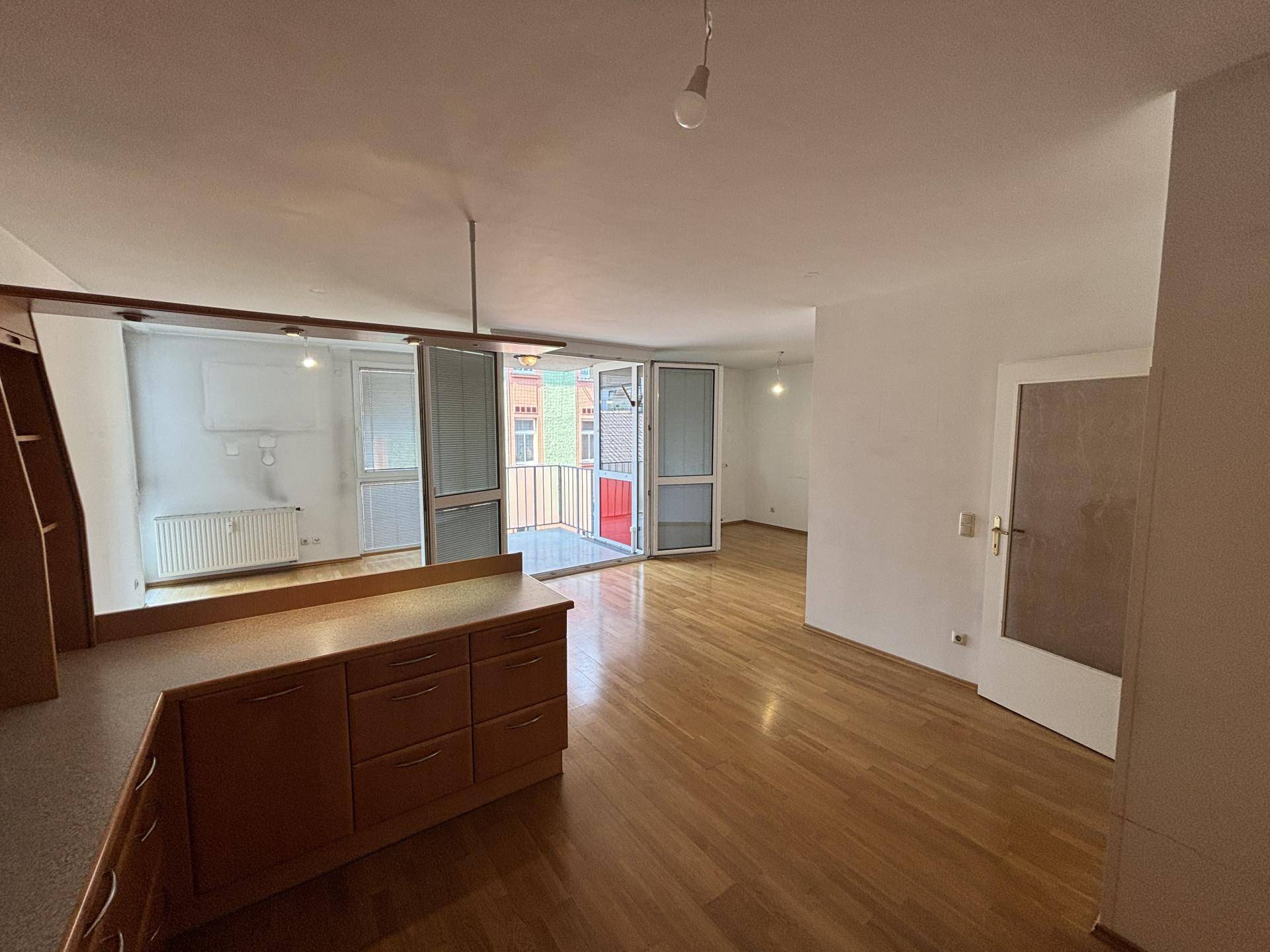 Heller, offener Wohnbereich mit Holzboden, semi-offener Küche und Zugang zu einem Balkon mit Stadtblick.