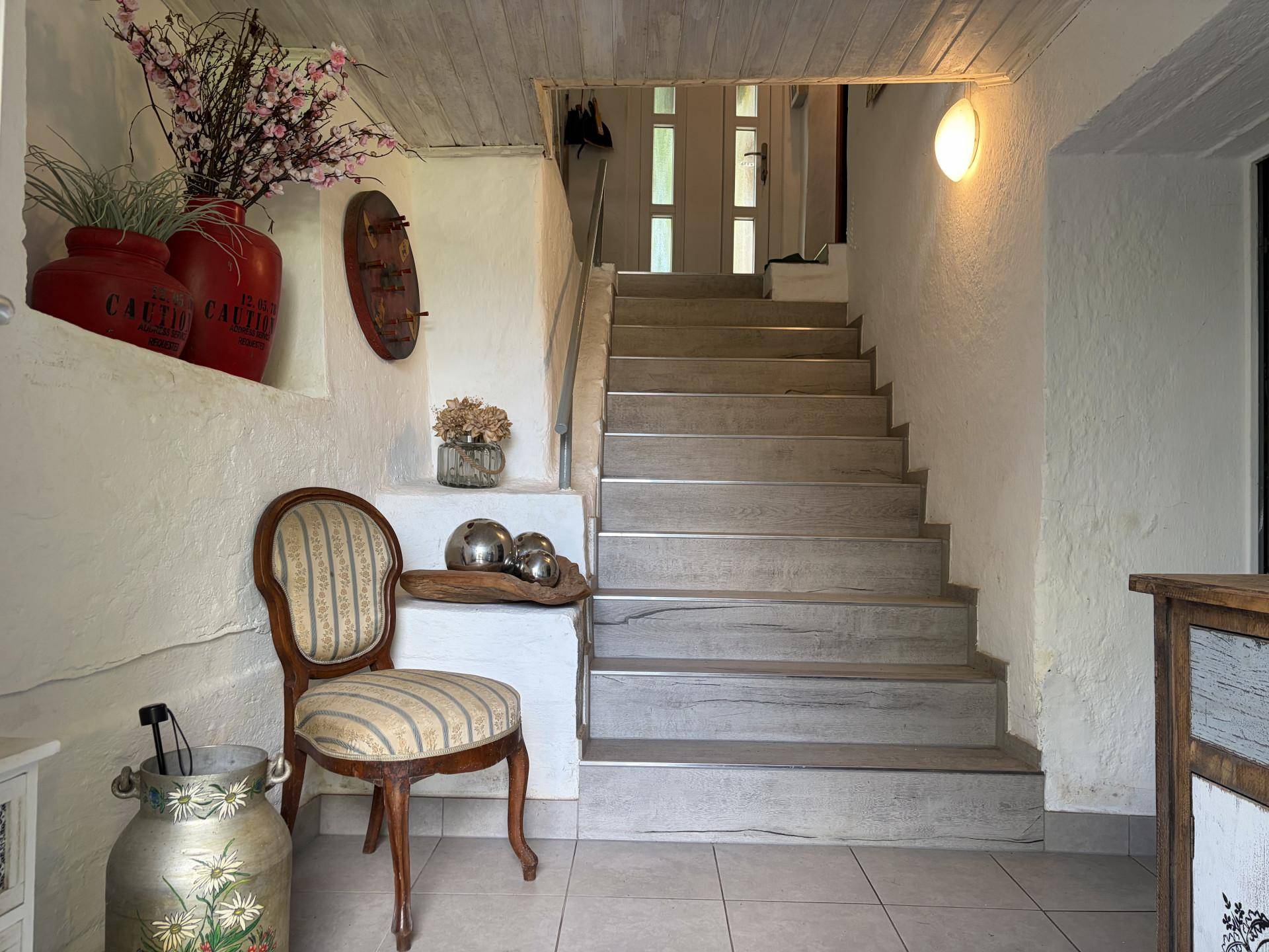 Heller Flur mit Treppe zum Obergeschoss, weiß getünchten Wänden und Holzakzenten.